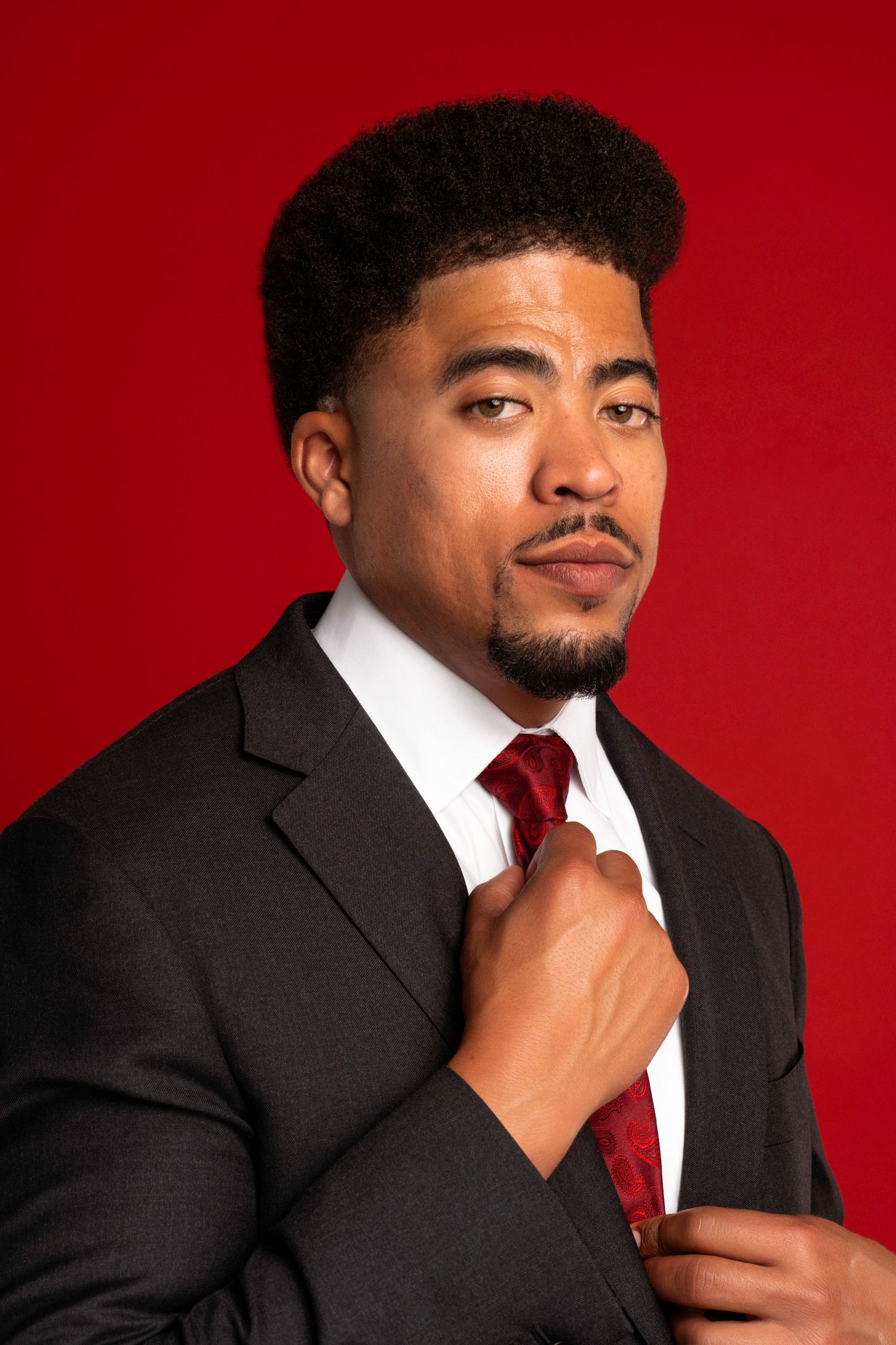 Professional portrait against red background wearing black suit and red tie.