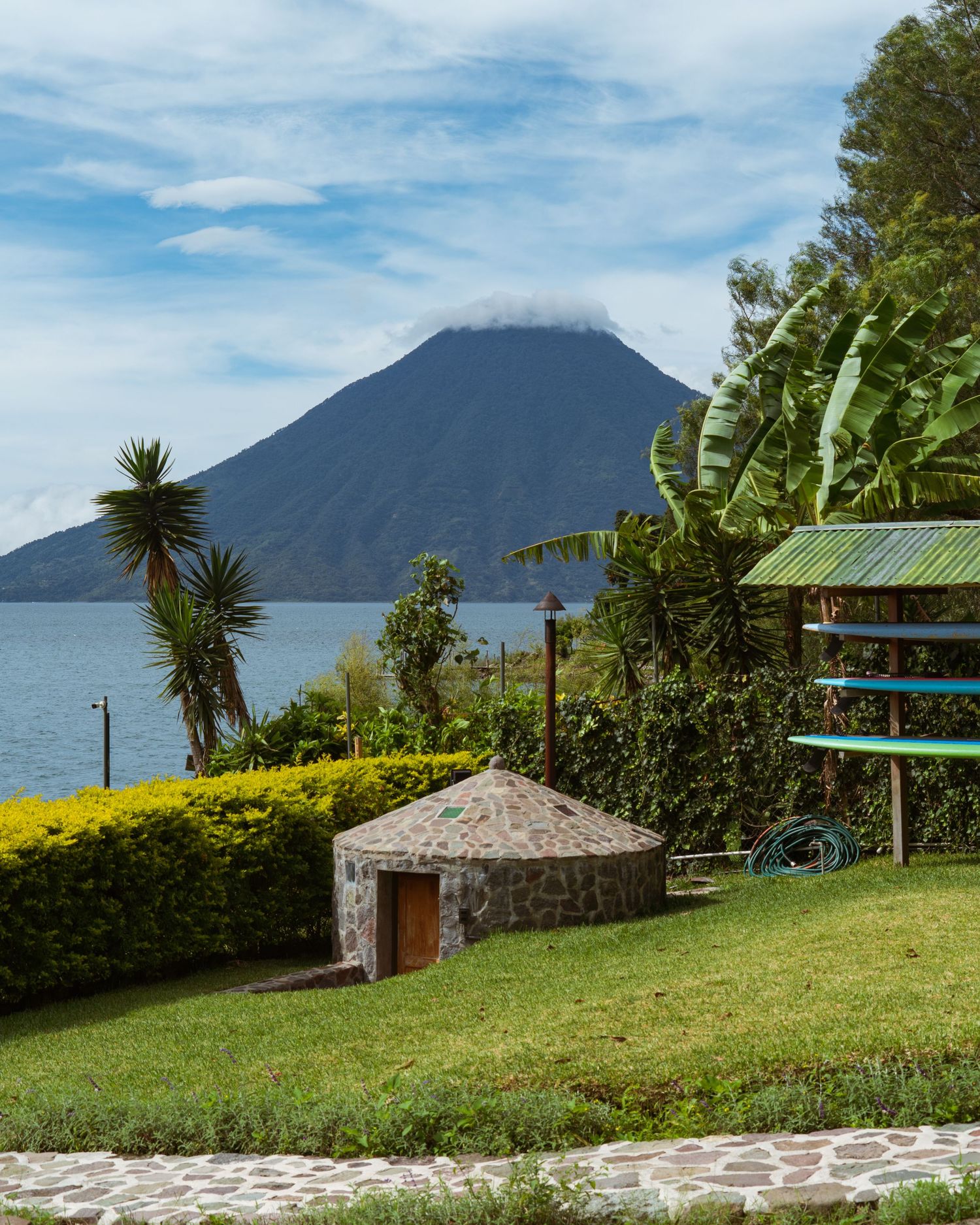 Landscaped garden with stone pathways overlooking Lake Atitlan and volcanic peaks.