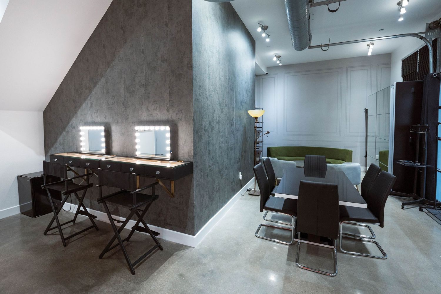 Modern makeup studio with vanity mirrors, black chairs, and a sleek grey conference area with leather seating.