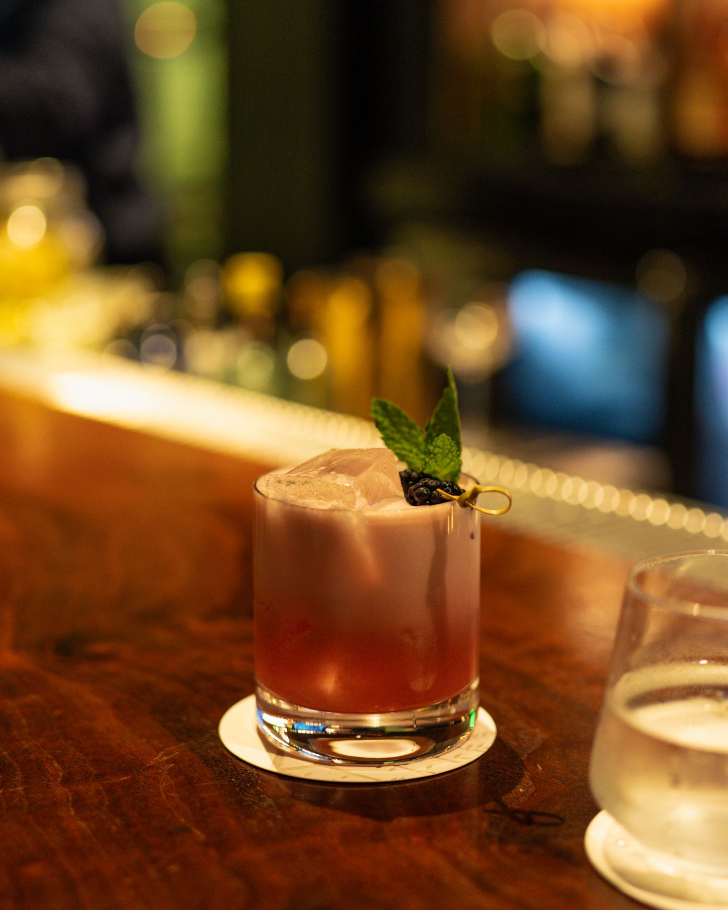 Craft cocktails with garnishes served on a dark wooden bar in moody lighting.