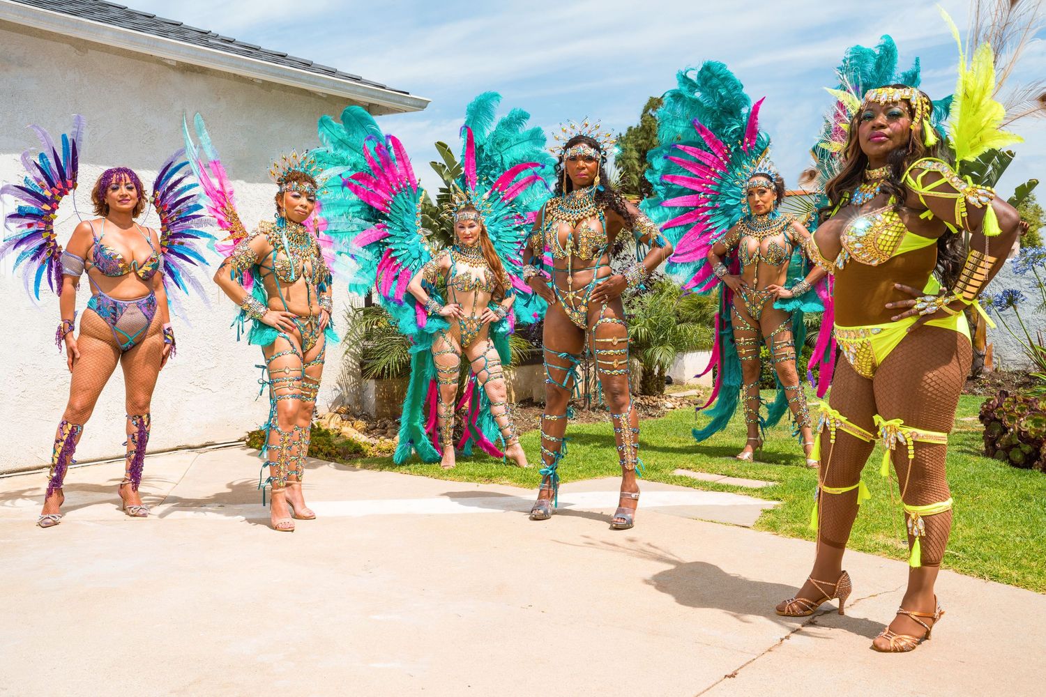 Group performance shot of carnival dancers in matching turquoise and pink feathered costumes.