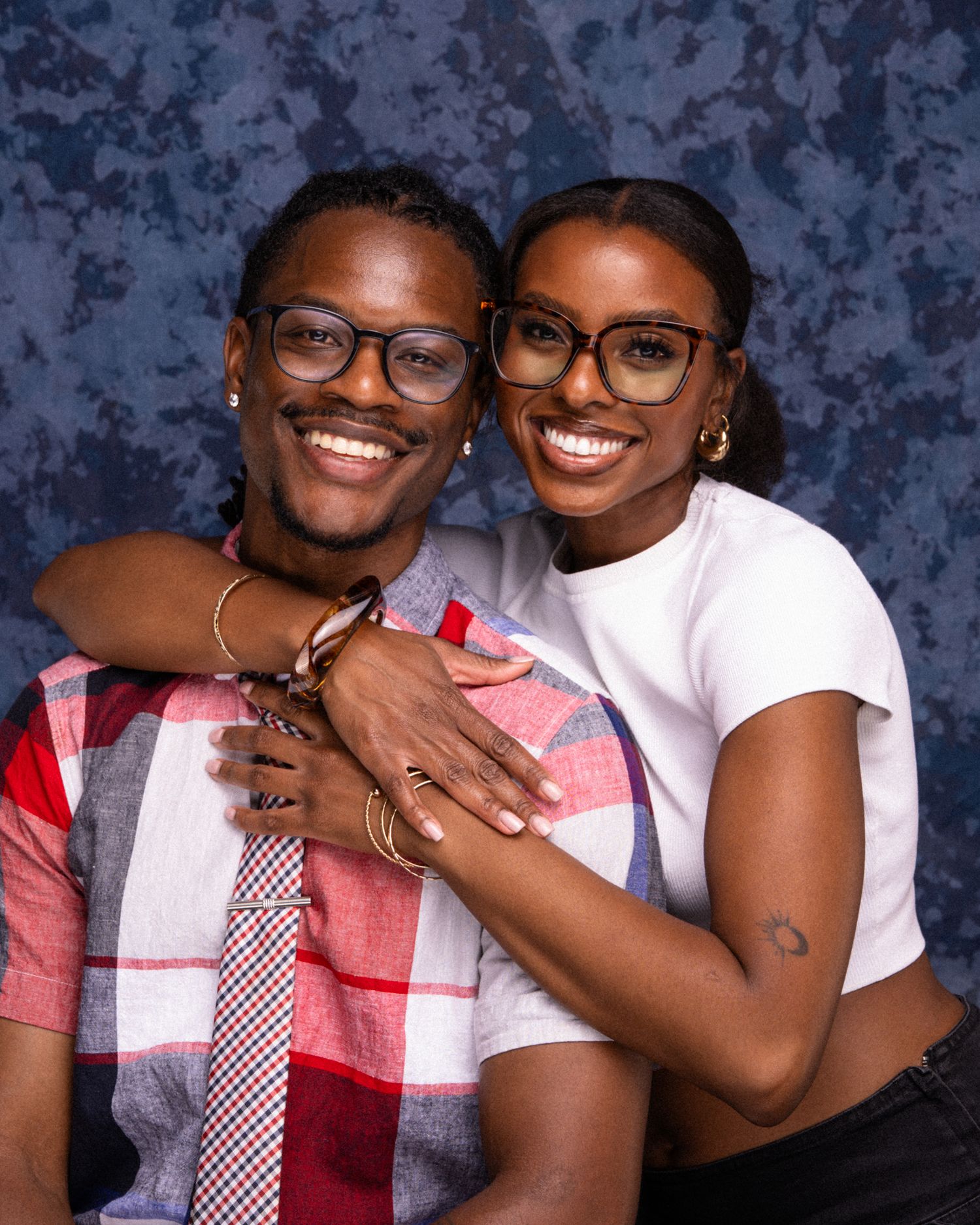 Two smiling people wearing glasses pose together affectionately in front of a blue backdrop.