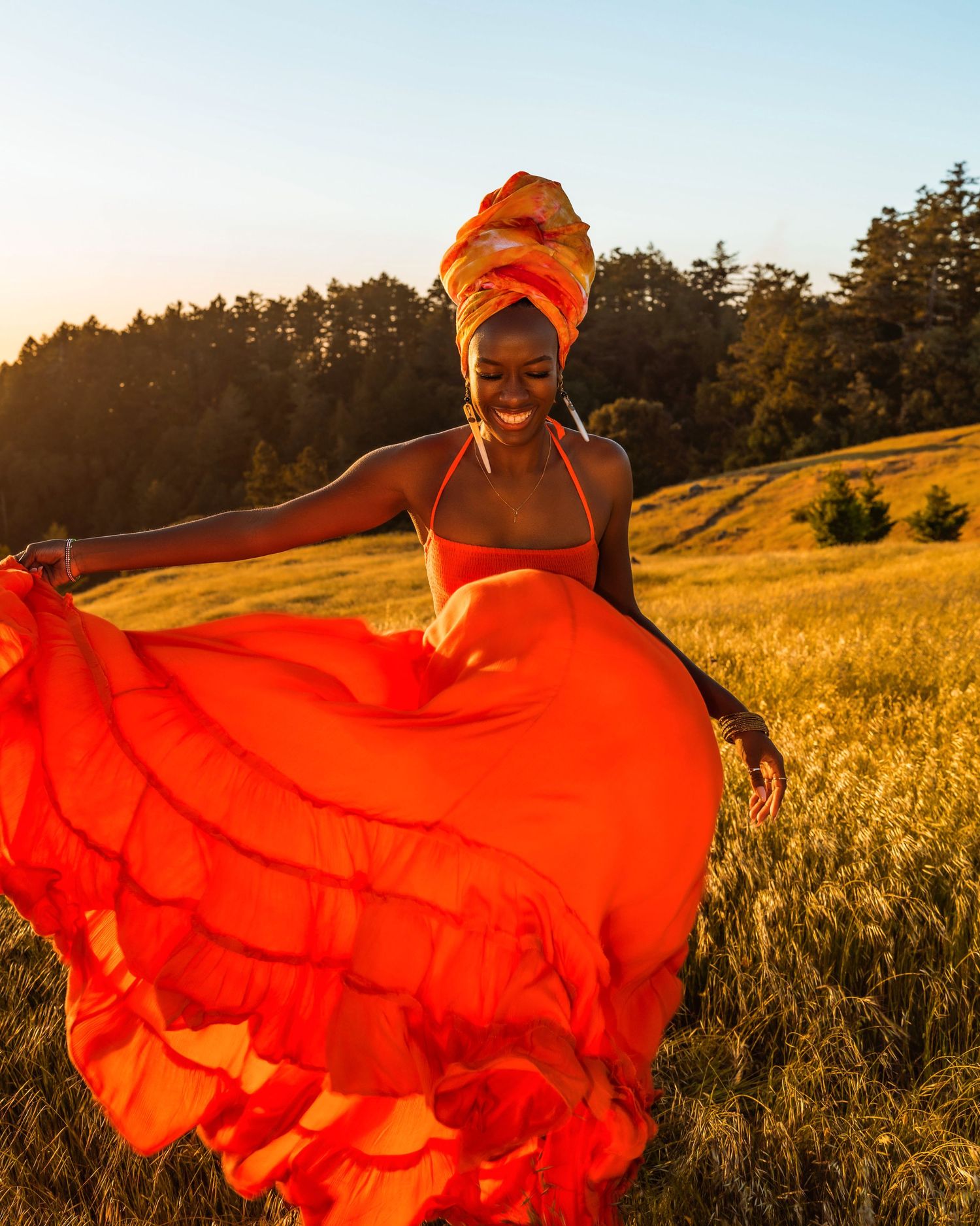 Woman in flowing red dress dancing gracefully in golden wheat field at sunset.
