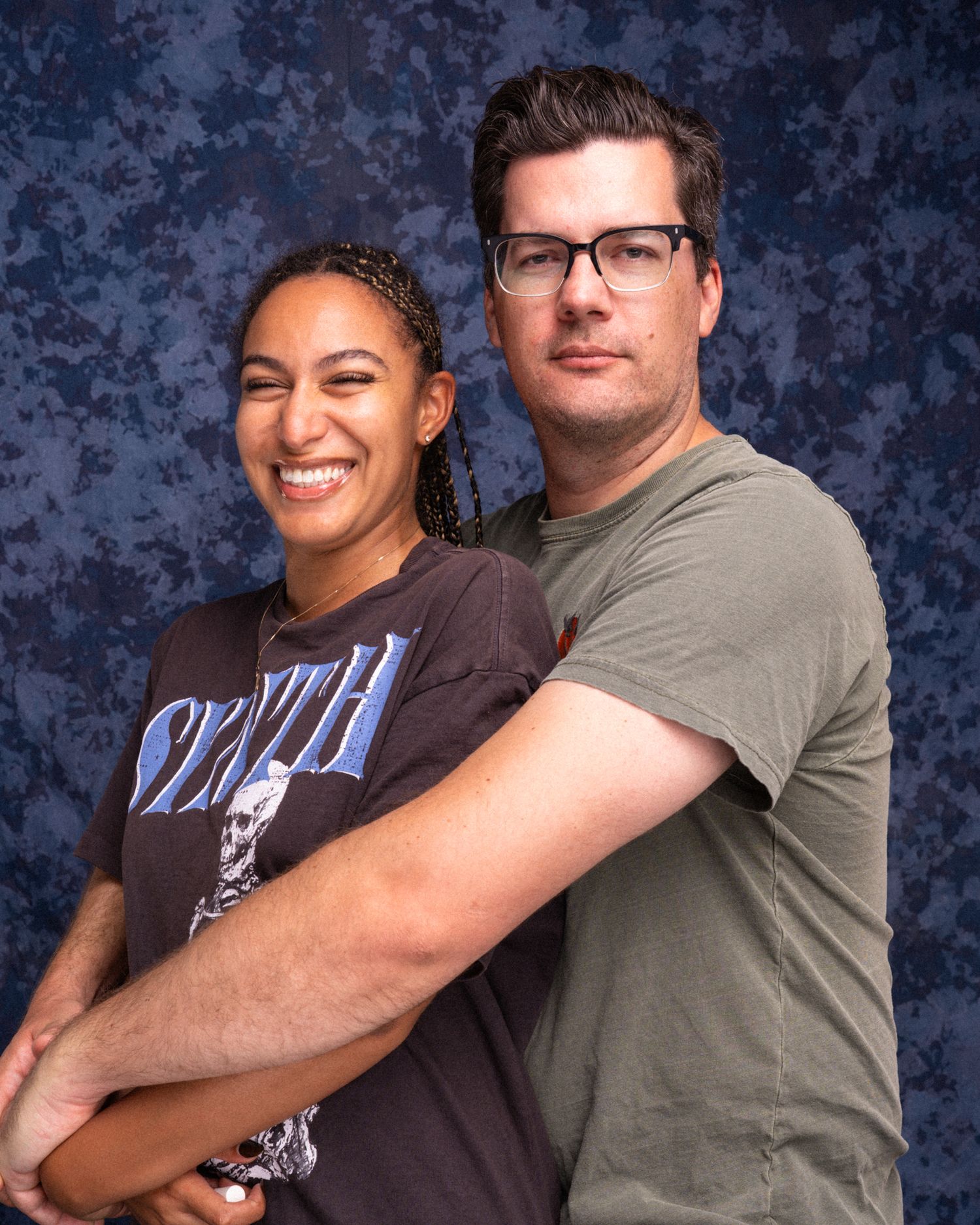 Two people smiling and embracing for a photo against a blue mottled background.