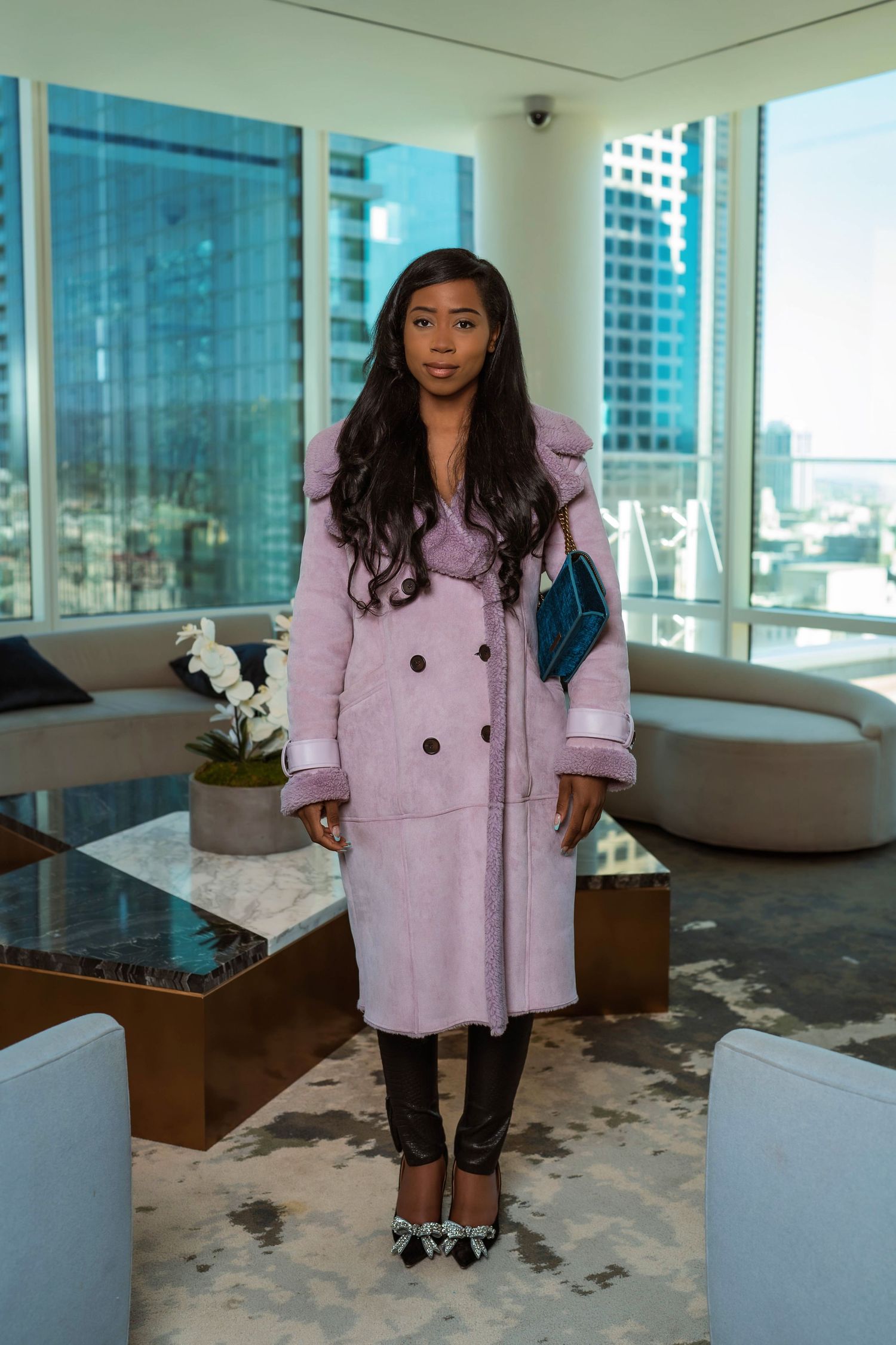 Professional fashion photoshoot in modern office space with pink coat against city skyline backdrop.