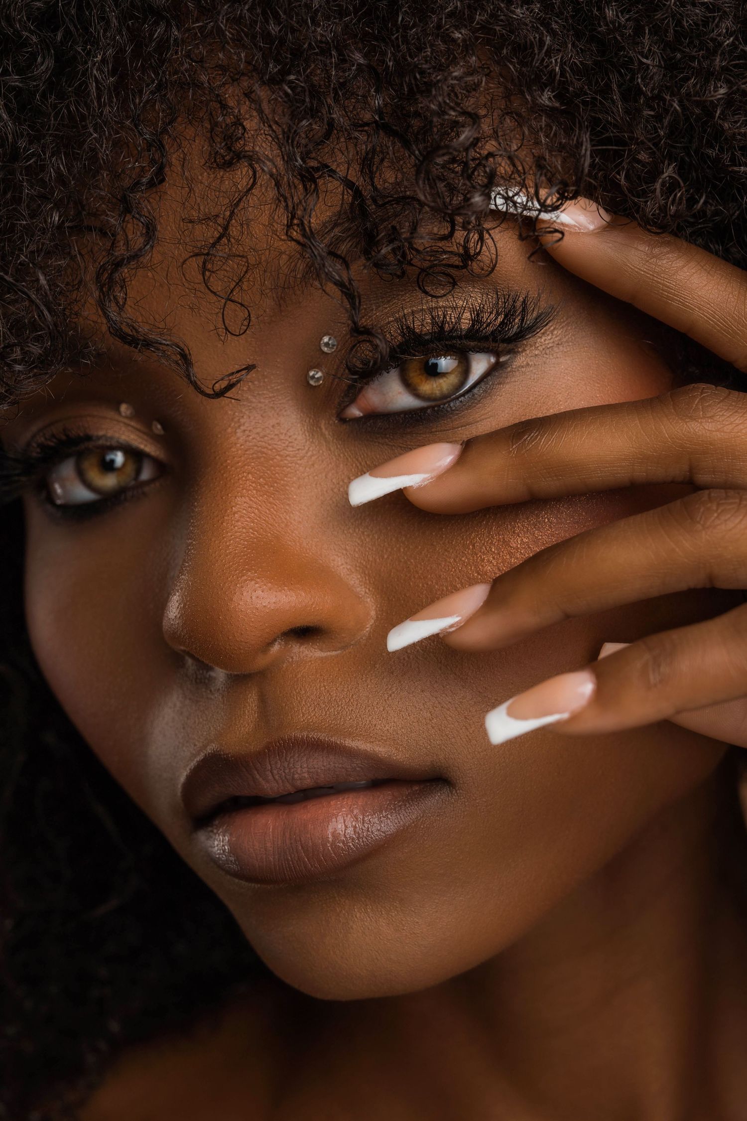 Artistic beauty portraits featuring white manicured nails and curly hair with dramatic eye makeup.