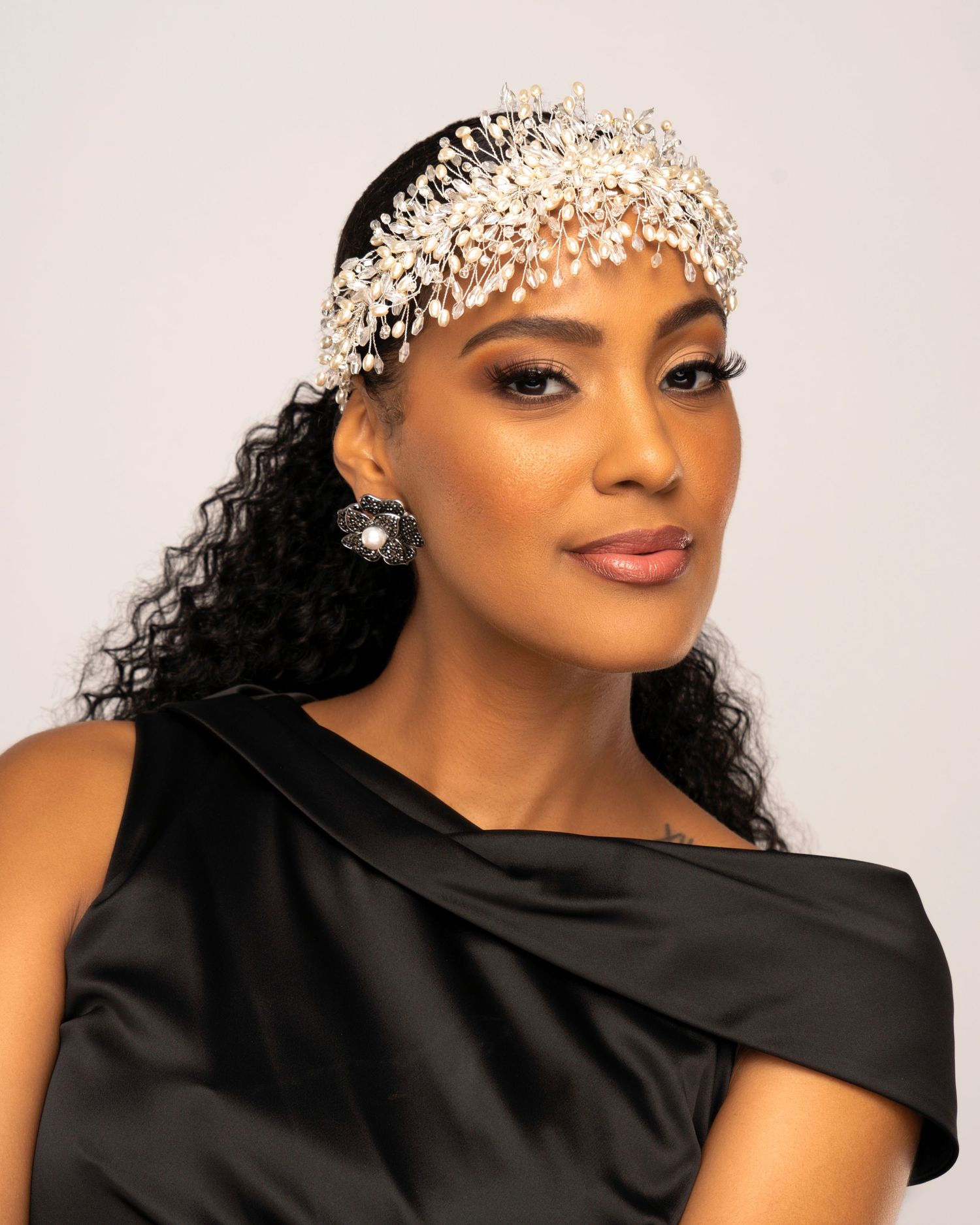 Elegant black evening gown look with pearl-adorned hair accessory in studio setting.