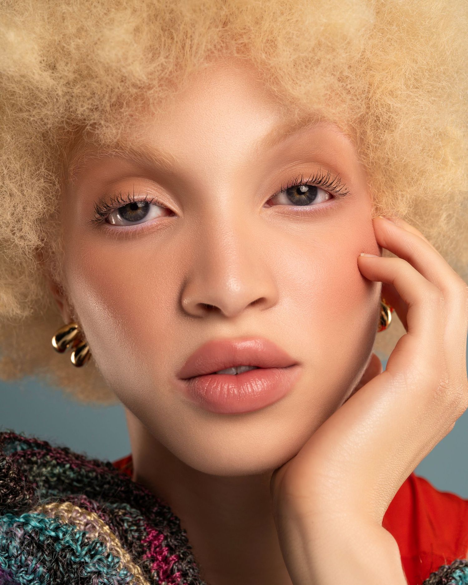 Close-up beauty shot with blonde afro and natural makeup against neutral background.