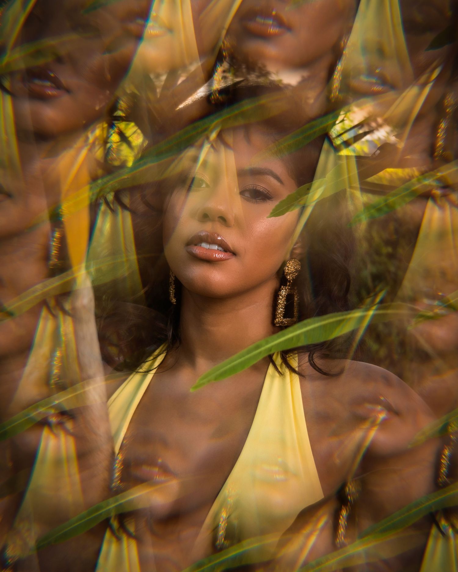 A woman in a yellow dress surrounded by tropical leaves in an artistic multiple exposure portrait photograph.