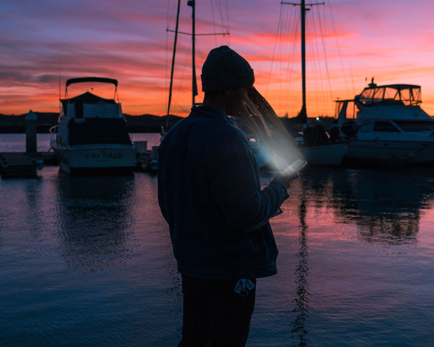 Scenic marina silhouette at sunset with boats and docks against a vibrant orange and purple sky.