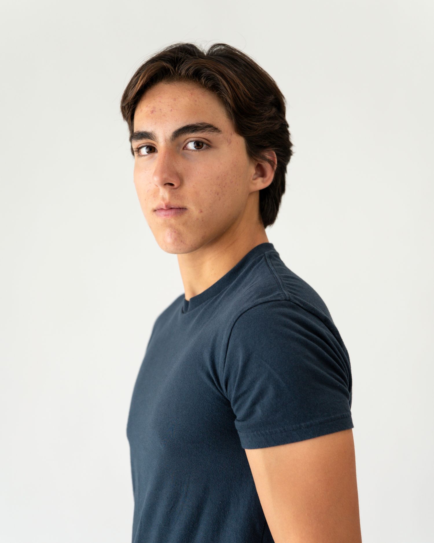 Young man with dark hair wearing a navy blue t-shirt poses against a white background.