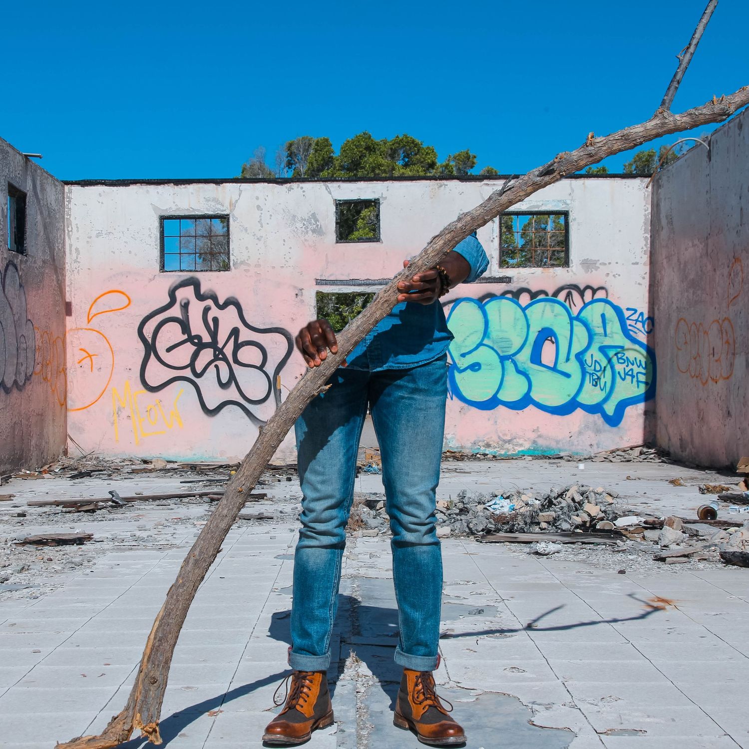 Creative perspective of legs in jeans against graffiti wall with leaning tree branch.
