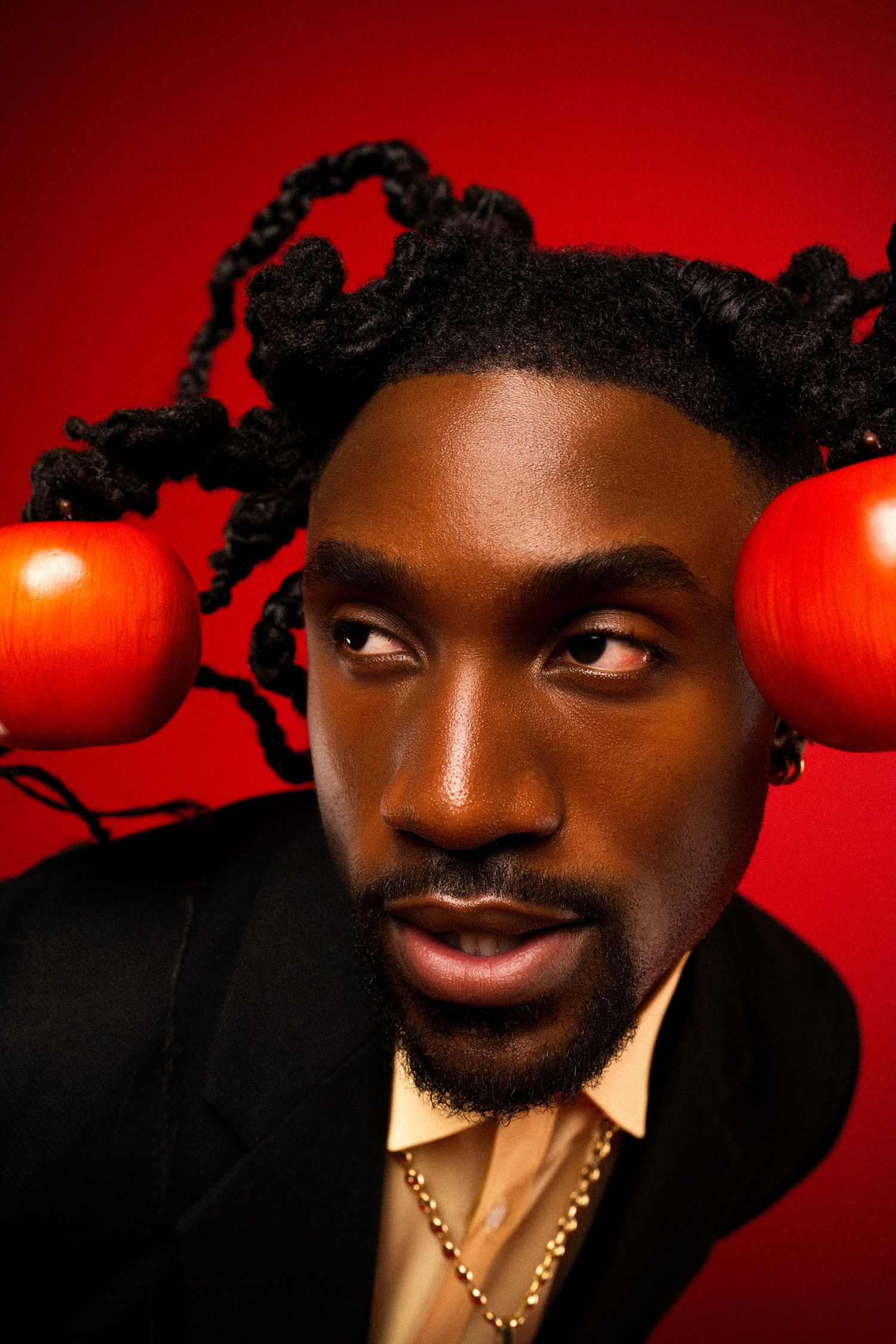 Close-up fashion portrait with red apples woven into braided hair against vibrant red background.