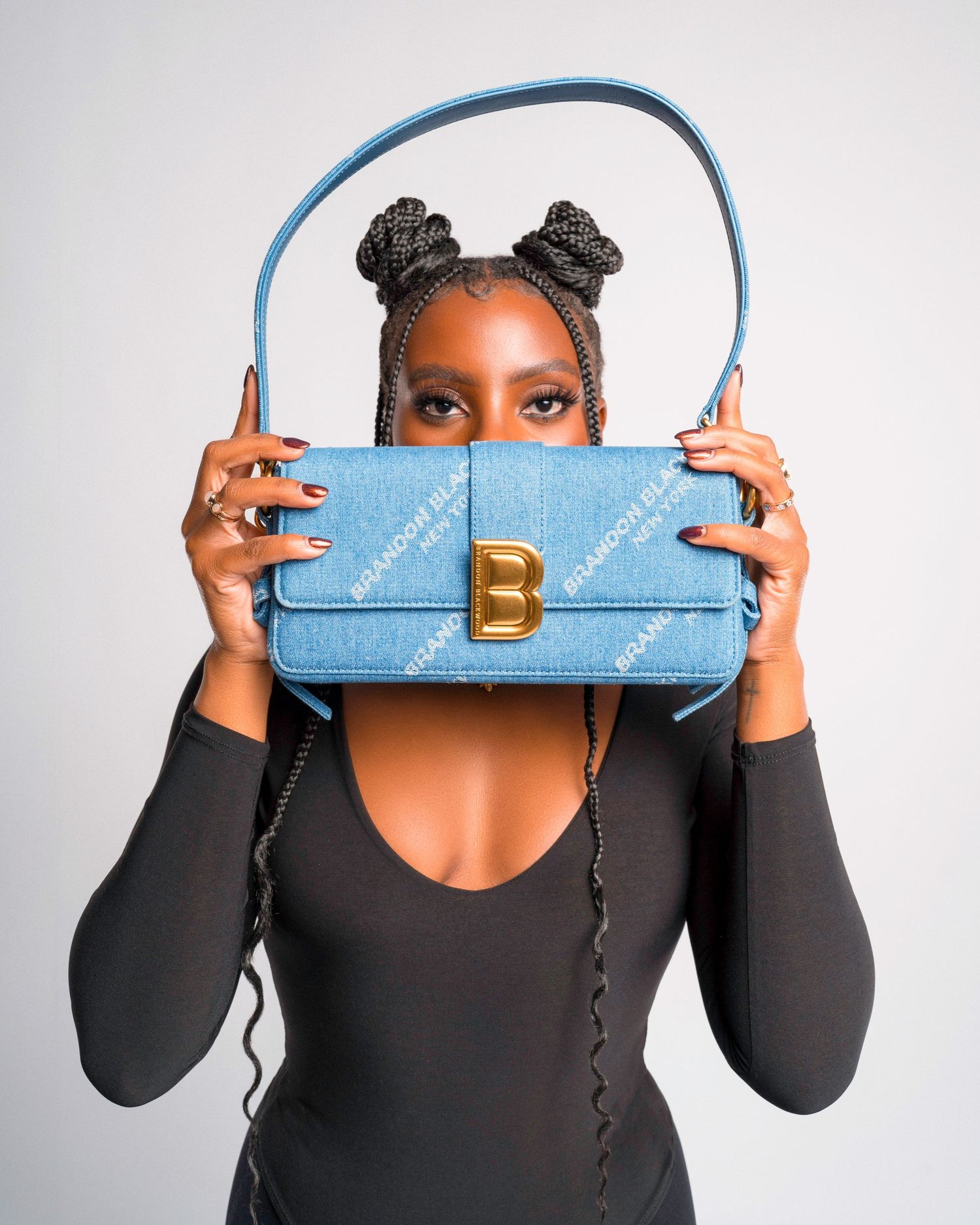 Stylish light blue handbag with gold B logo held up against black outfit in fashion product photo.