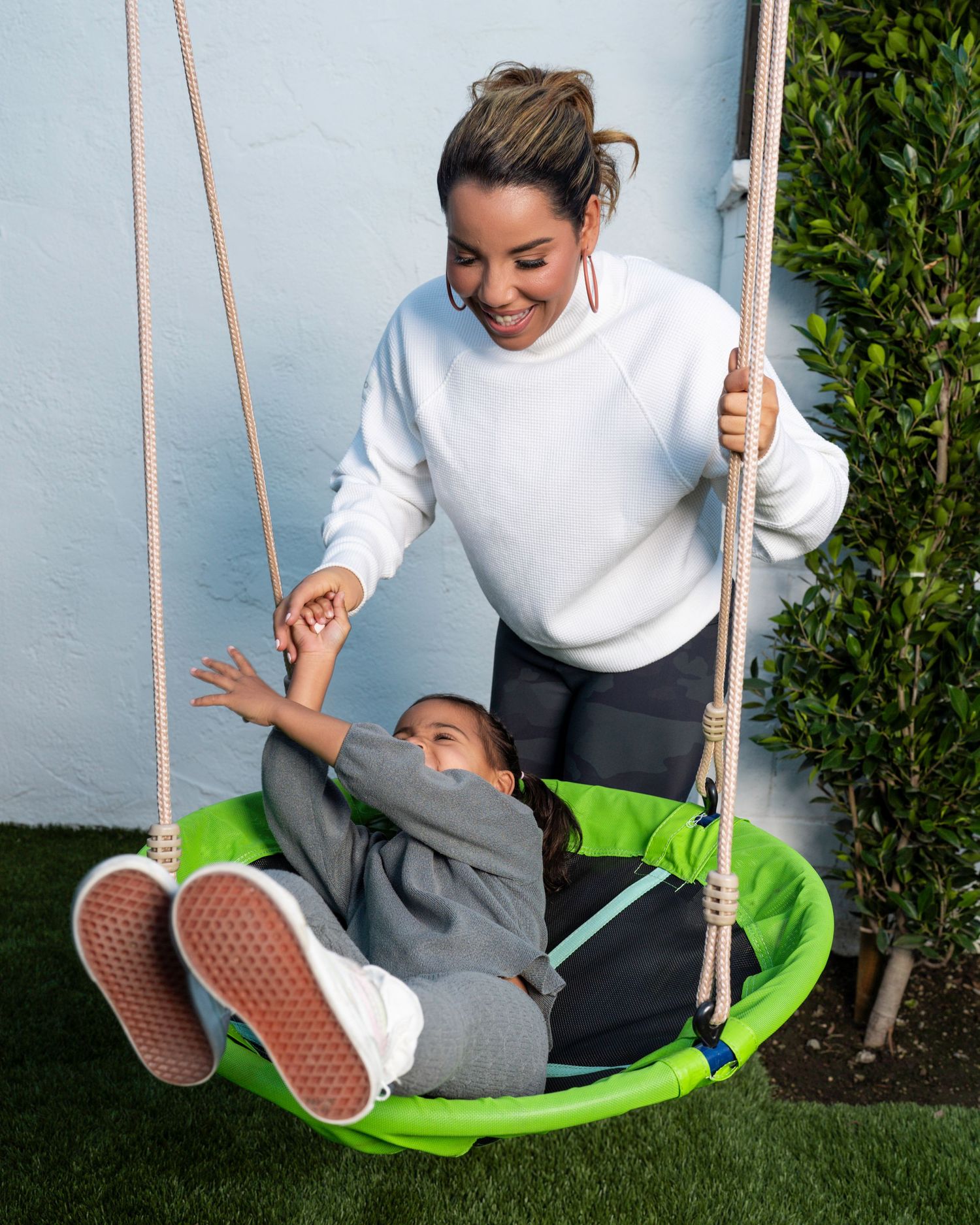 Playful moment on outdoor swing set with white sweater and joyful expressions.
