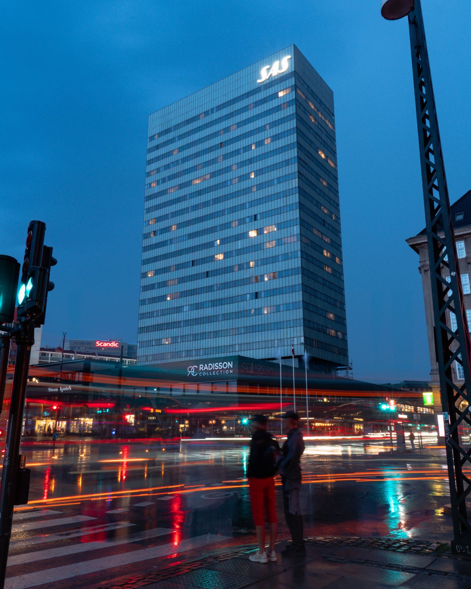 Modern glass office building illuminated at night with light trails from passing traffic.