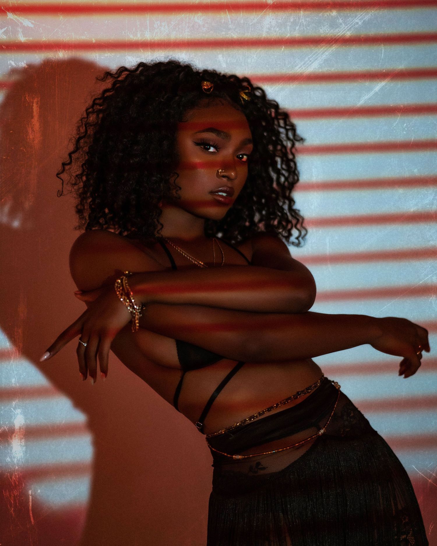 Moody boudoir photoshoot with venetian blind lighting effects creating dramatic shadows.