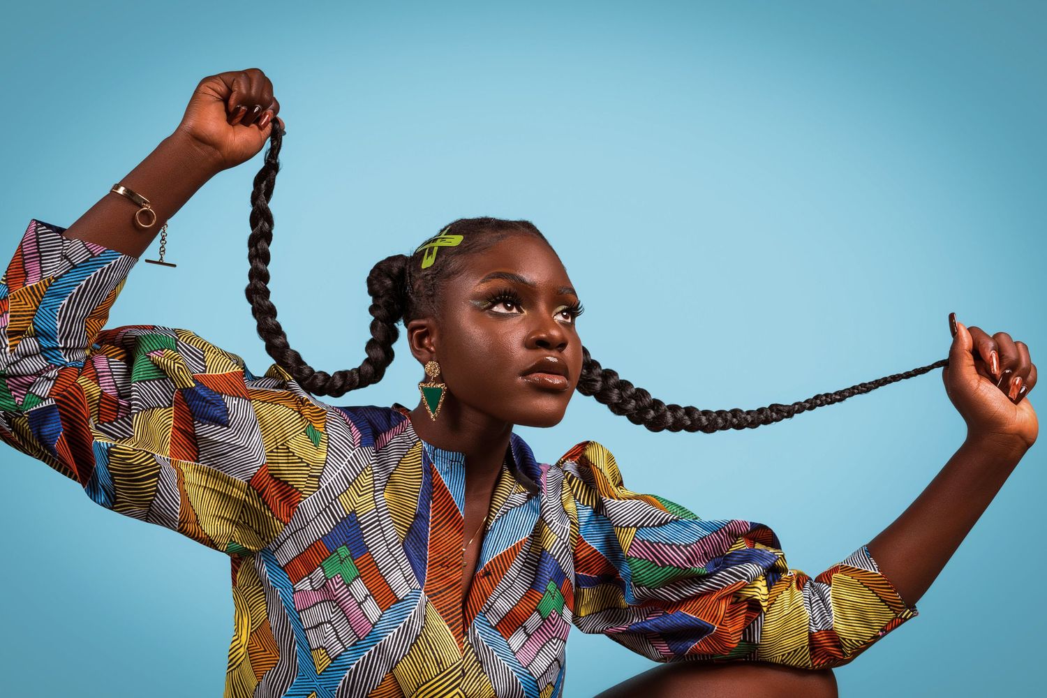 Fashion portrait with vibrant patterned shirt and long braids against blue background.