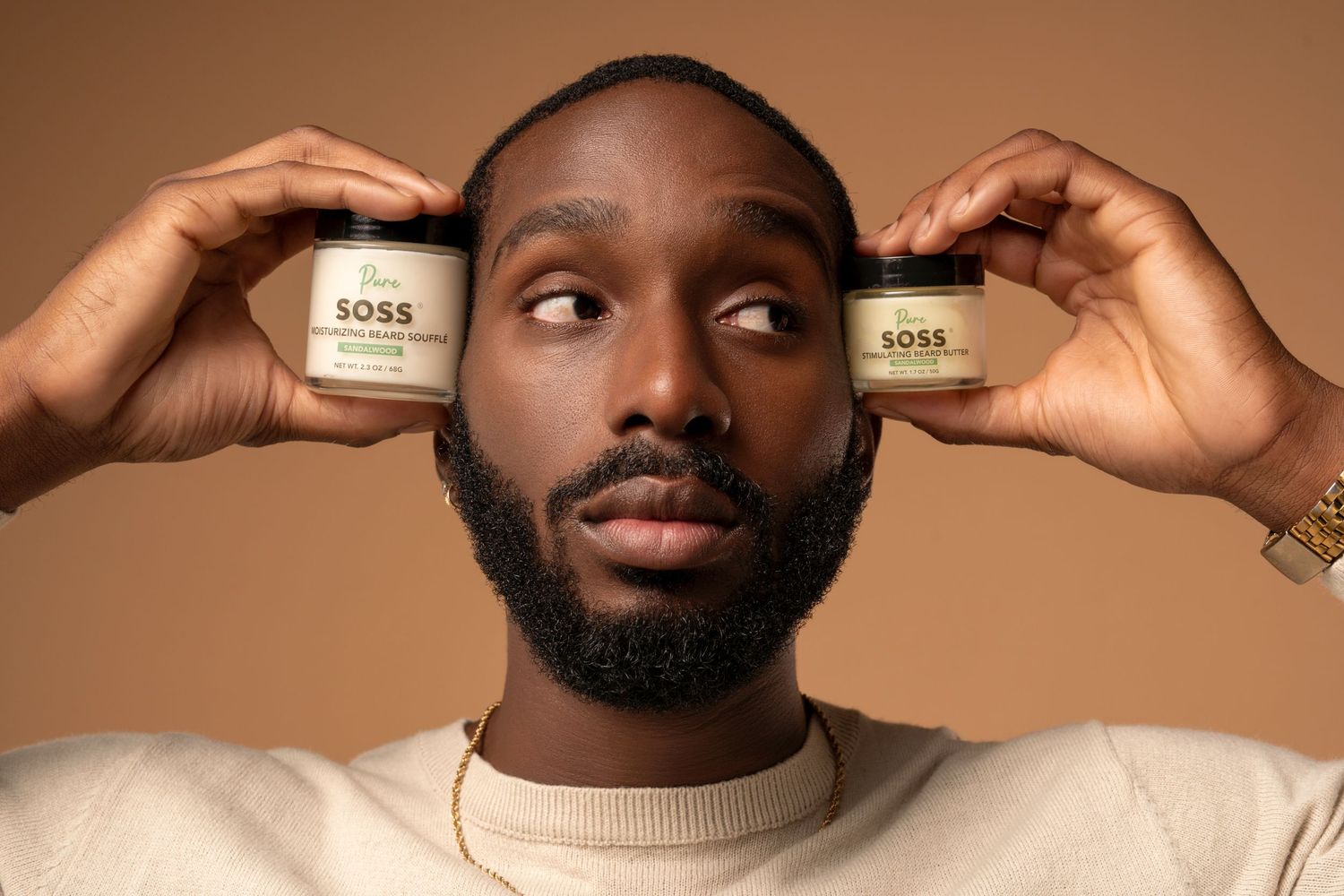 Person holding two jars of SOSS skincare products beside their face.