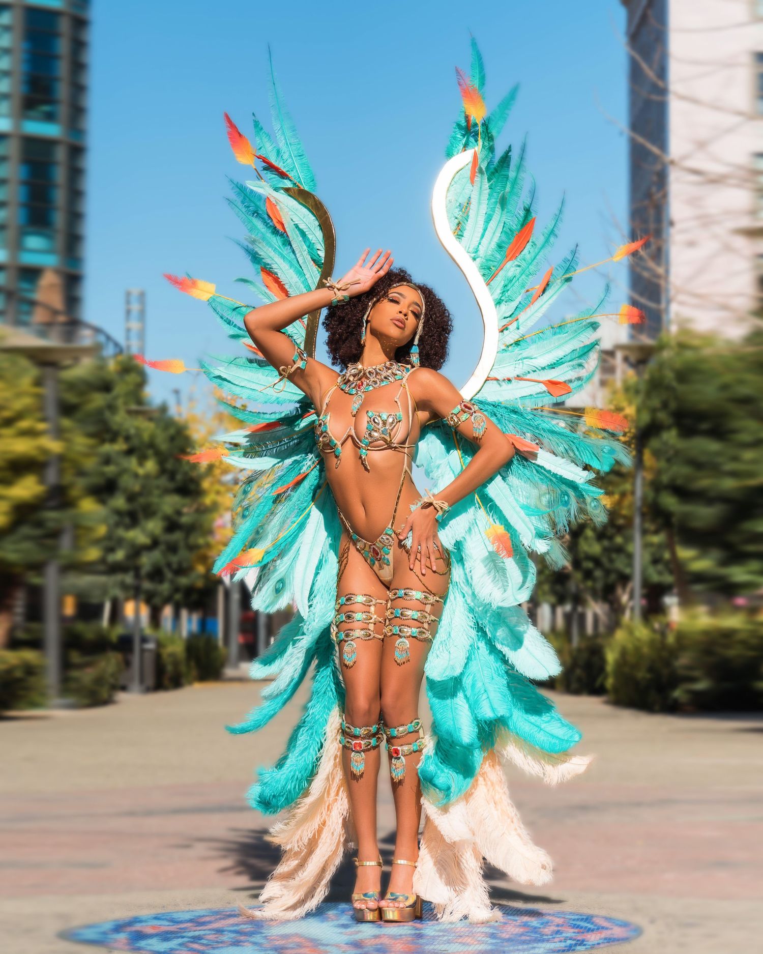 Carnival performer in turquoise feathered wings dancing outdoors in urban setting.