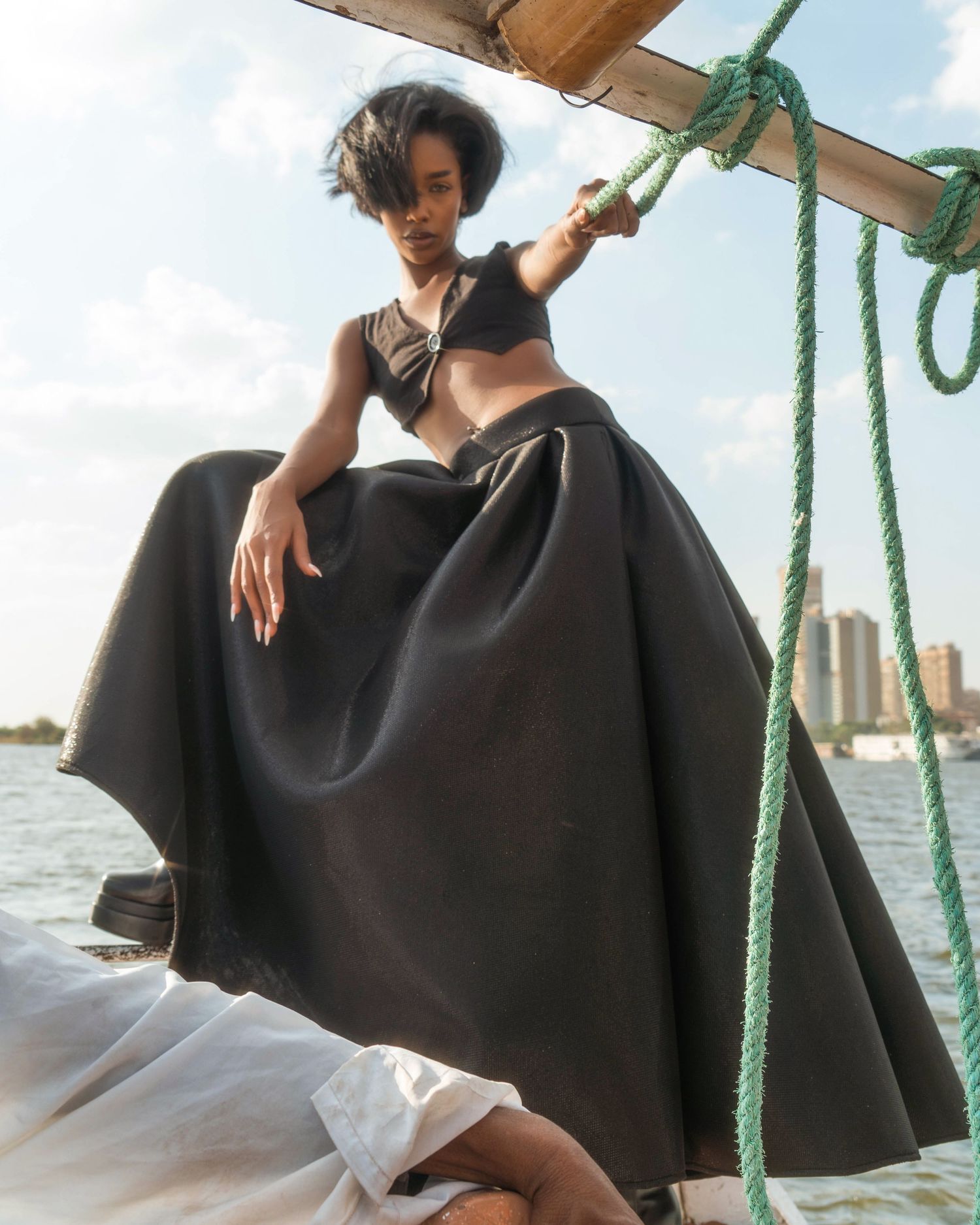 Model in flowing black cape dress poses on sailboat deck.