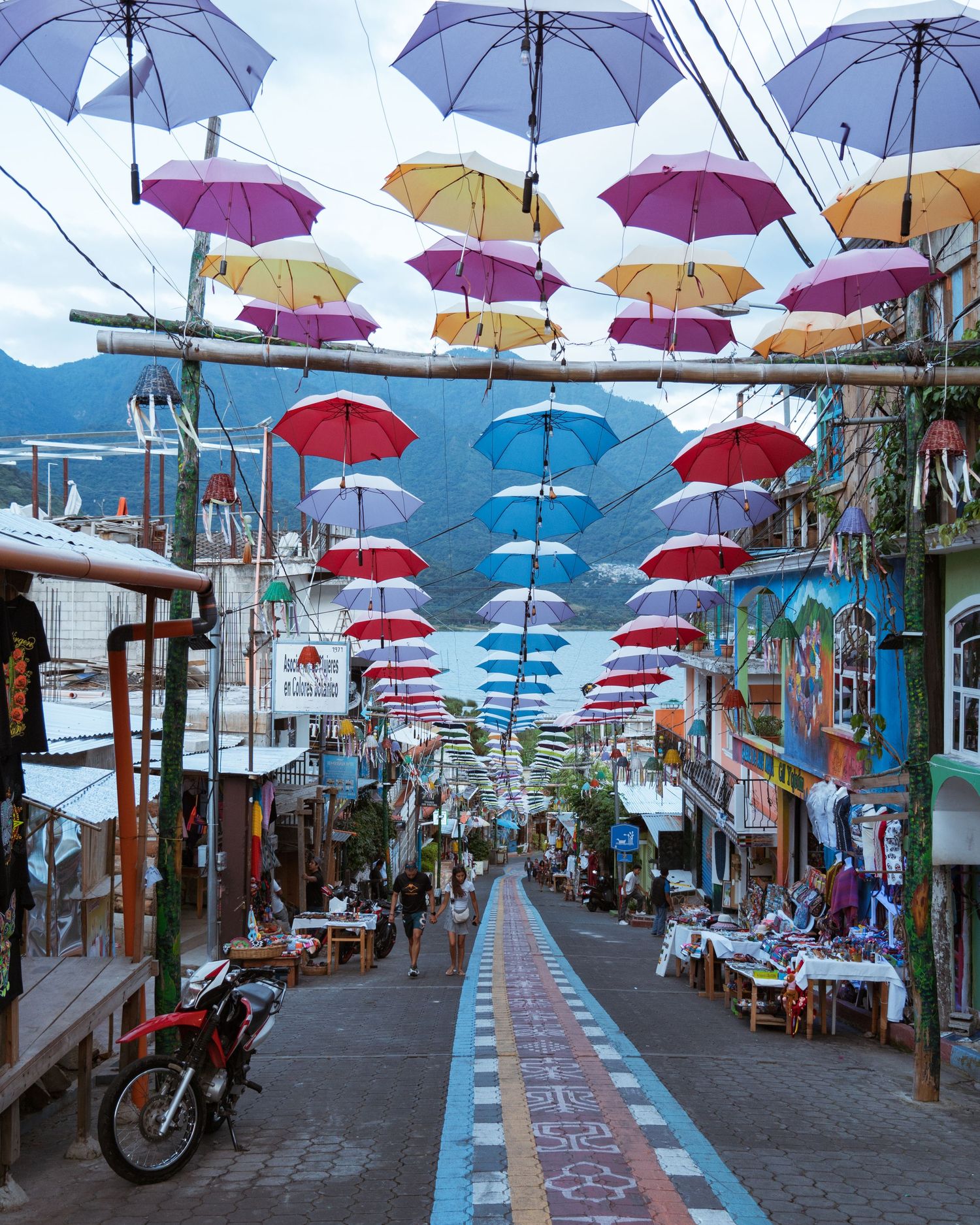 Charming street decorated with colorful hanging umbrellas against a mountain backdrop.