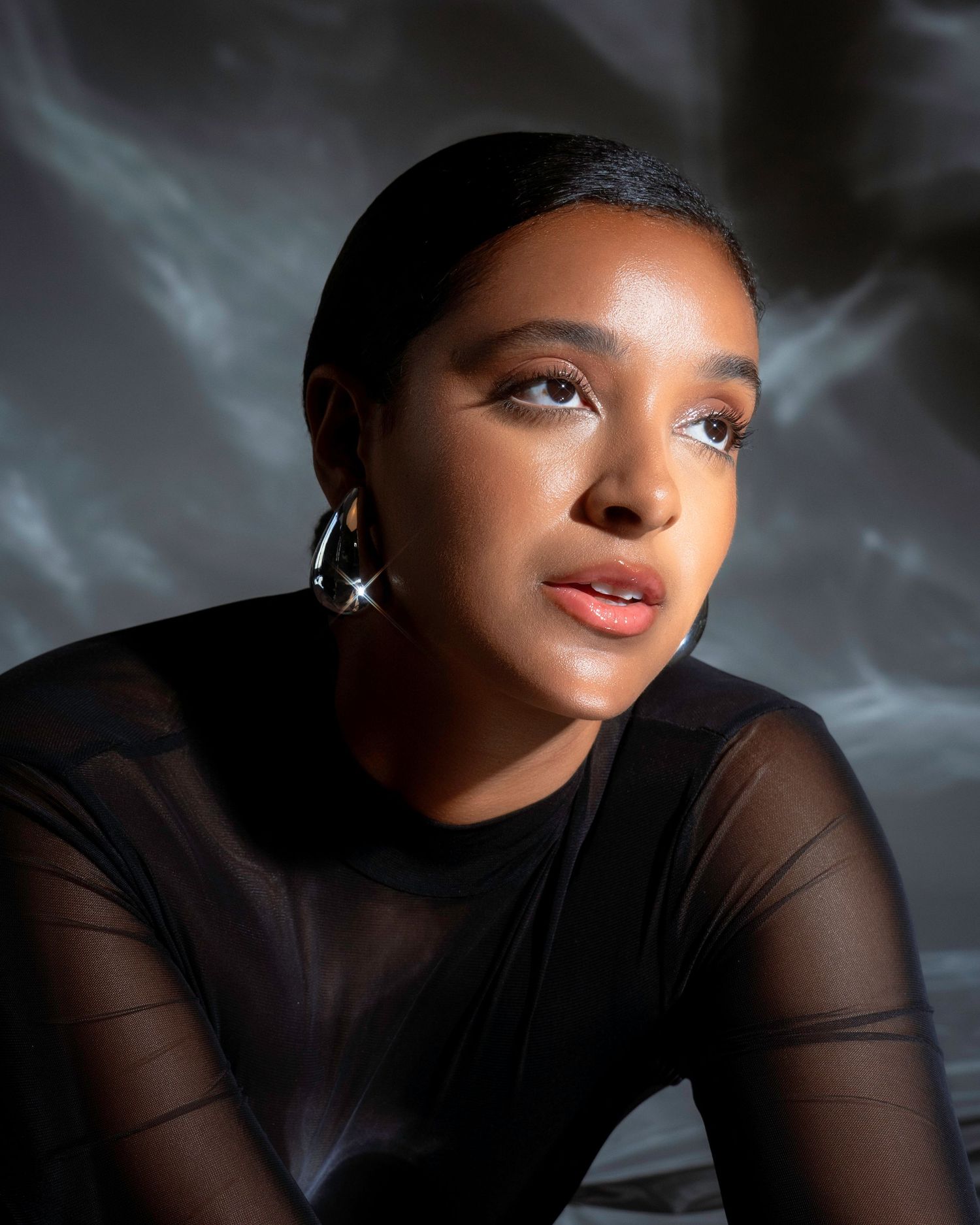 Close up beauty shot with shimmering makeup and sparkling earrings against smoky background.