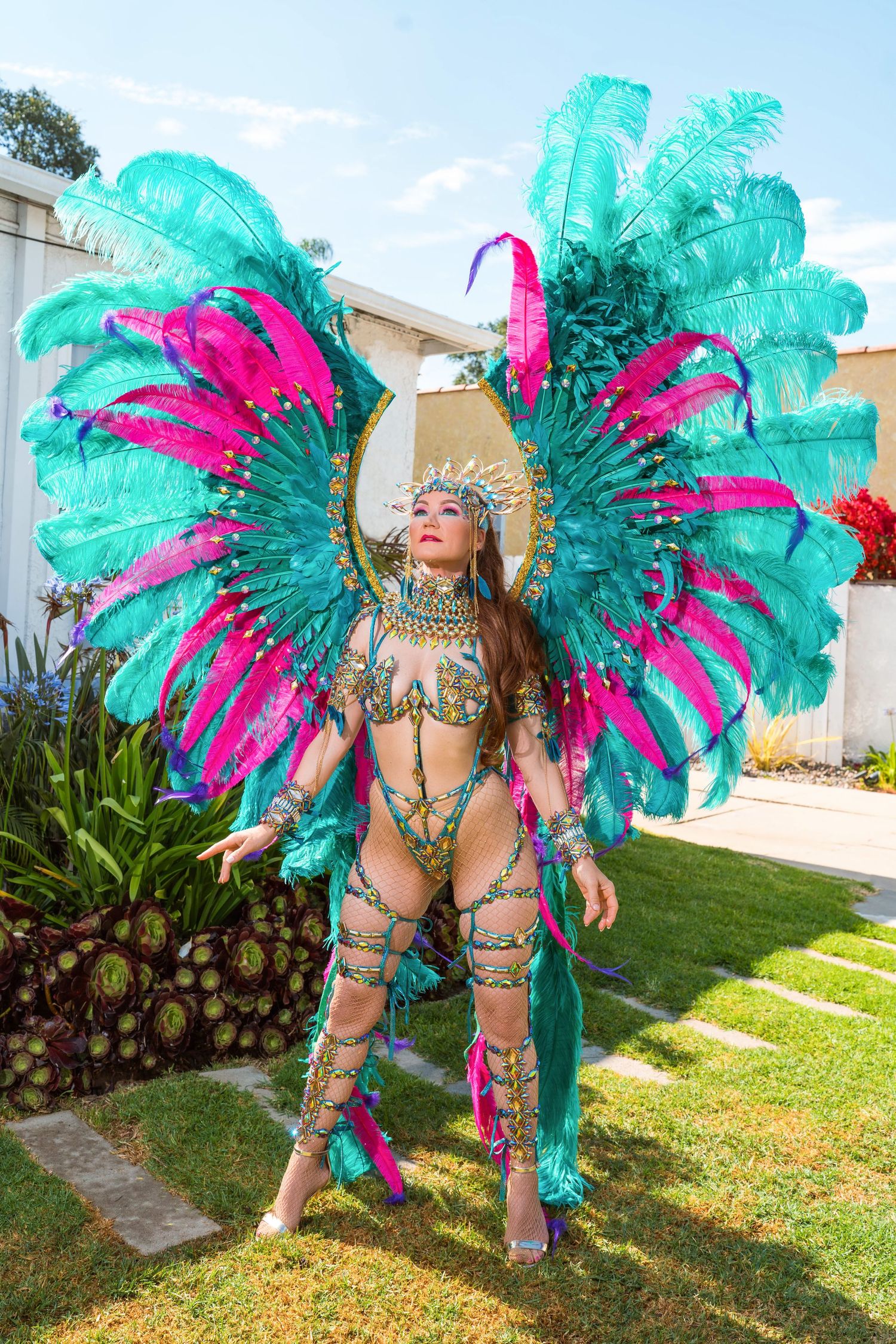 Elaborate carnival dancer costume featuring bright turquoise and pink feathers against outdoor backdrop.