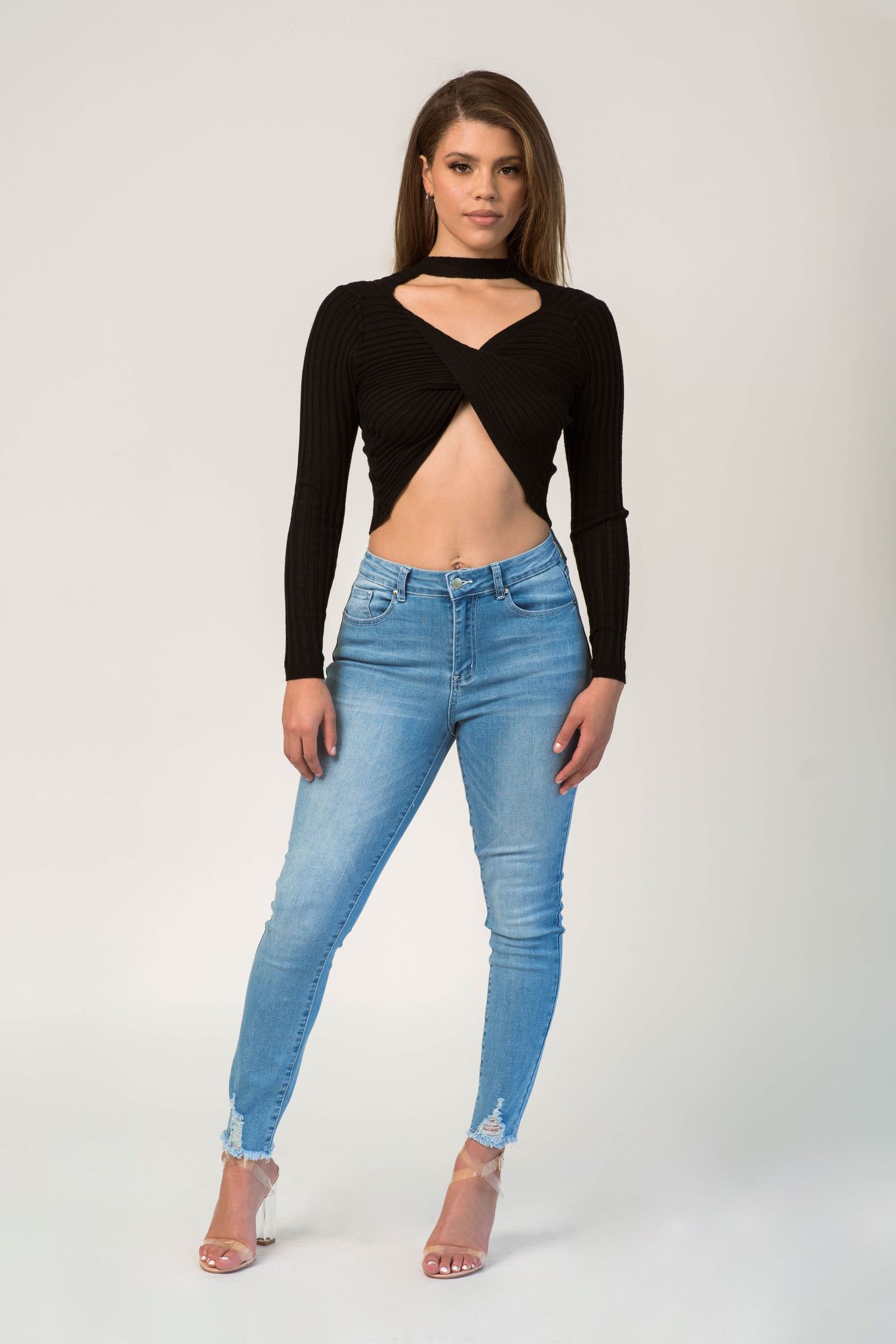 Fashion model wearing distressed light blue jeans and black crop top in studio setting.