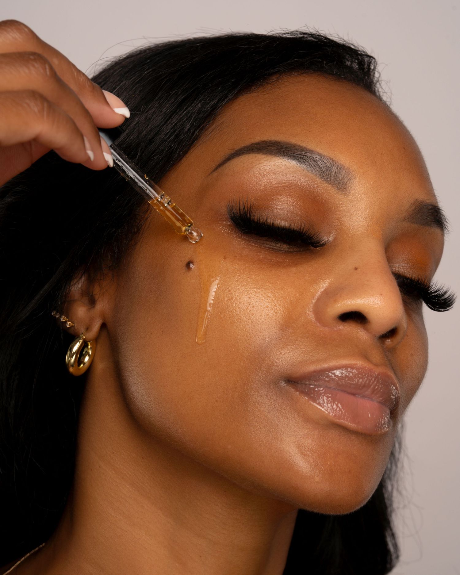 Close-up of beauty product being applied with dropper on glowing skin.