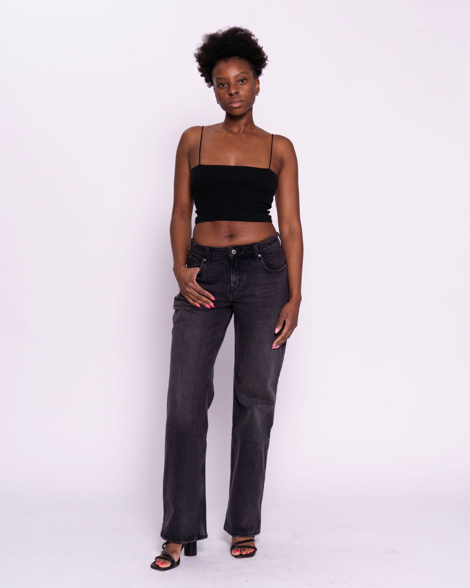 Woman wearing black crop top and dark gray wide-leg jeans with black heeled sandals on white background.