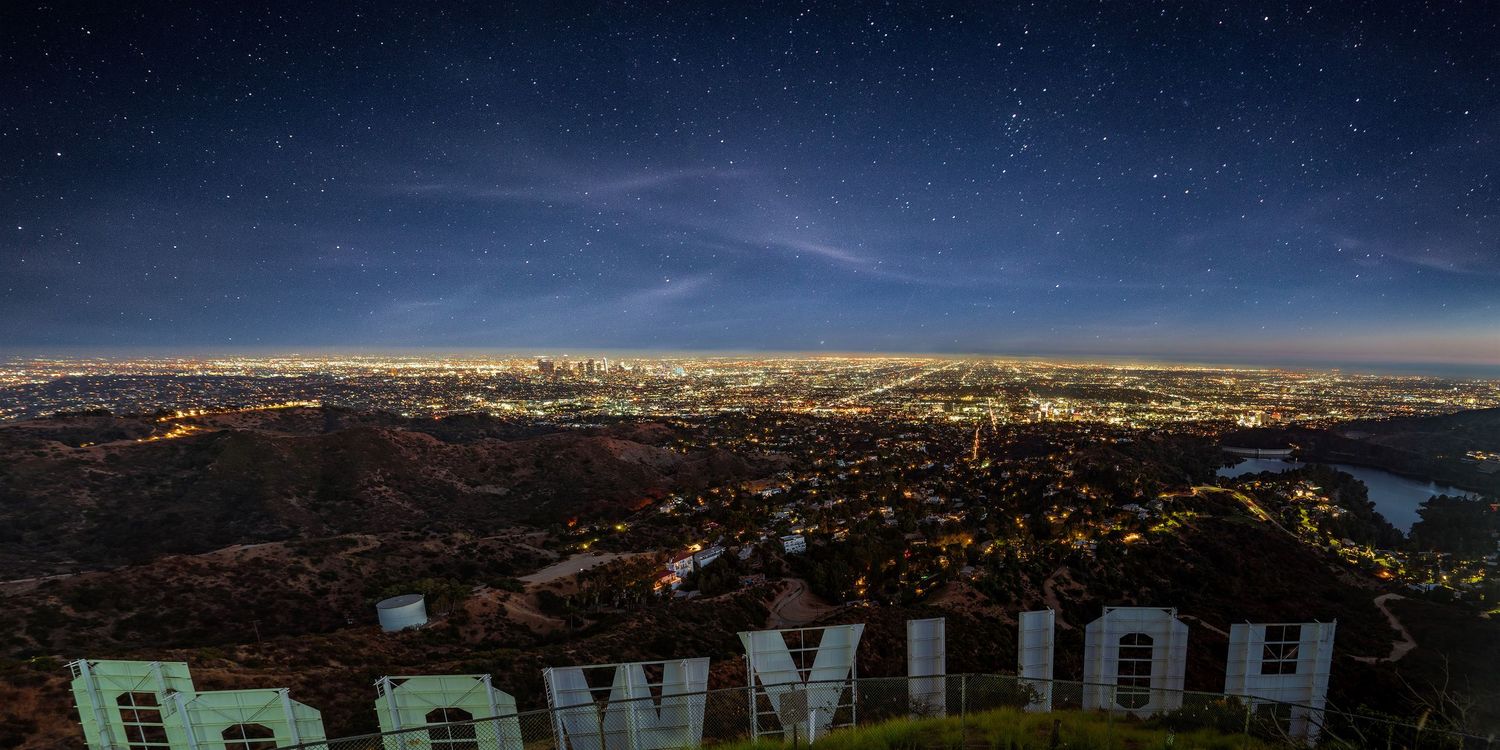 Panoramic nighttime cityscape view with Hollywood sign and starry sky.