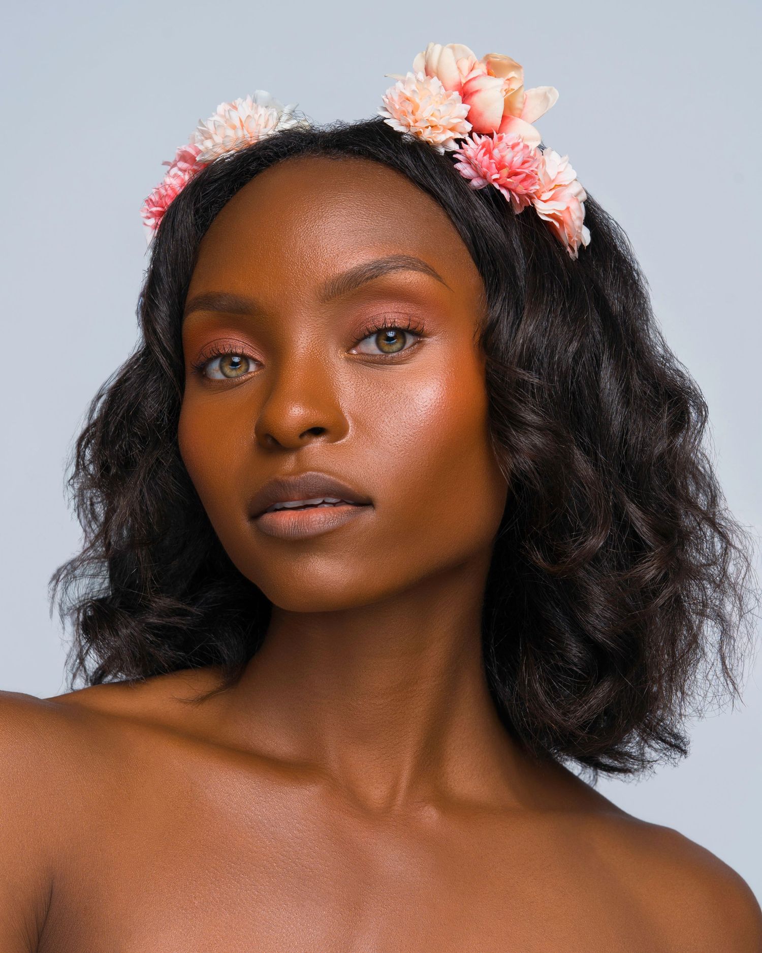 Ethereal beauty shot with coral flowers adorning wavy dark hair.