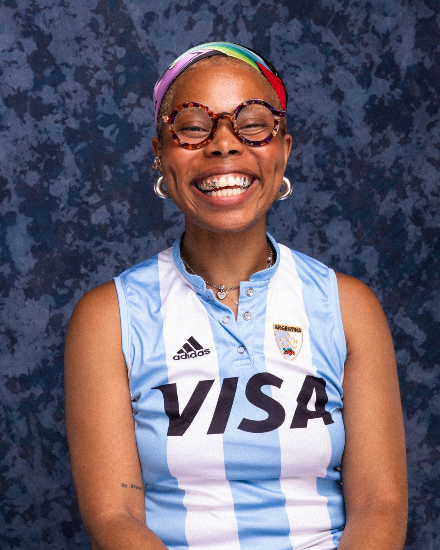 Smiling woman in Adidas VISA jersey wearing colorful glasses and headband.