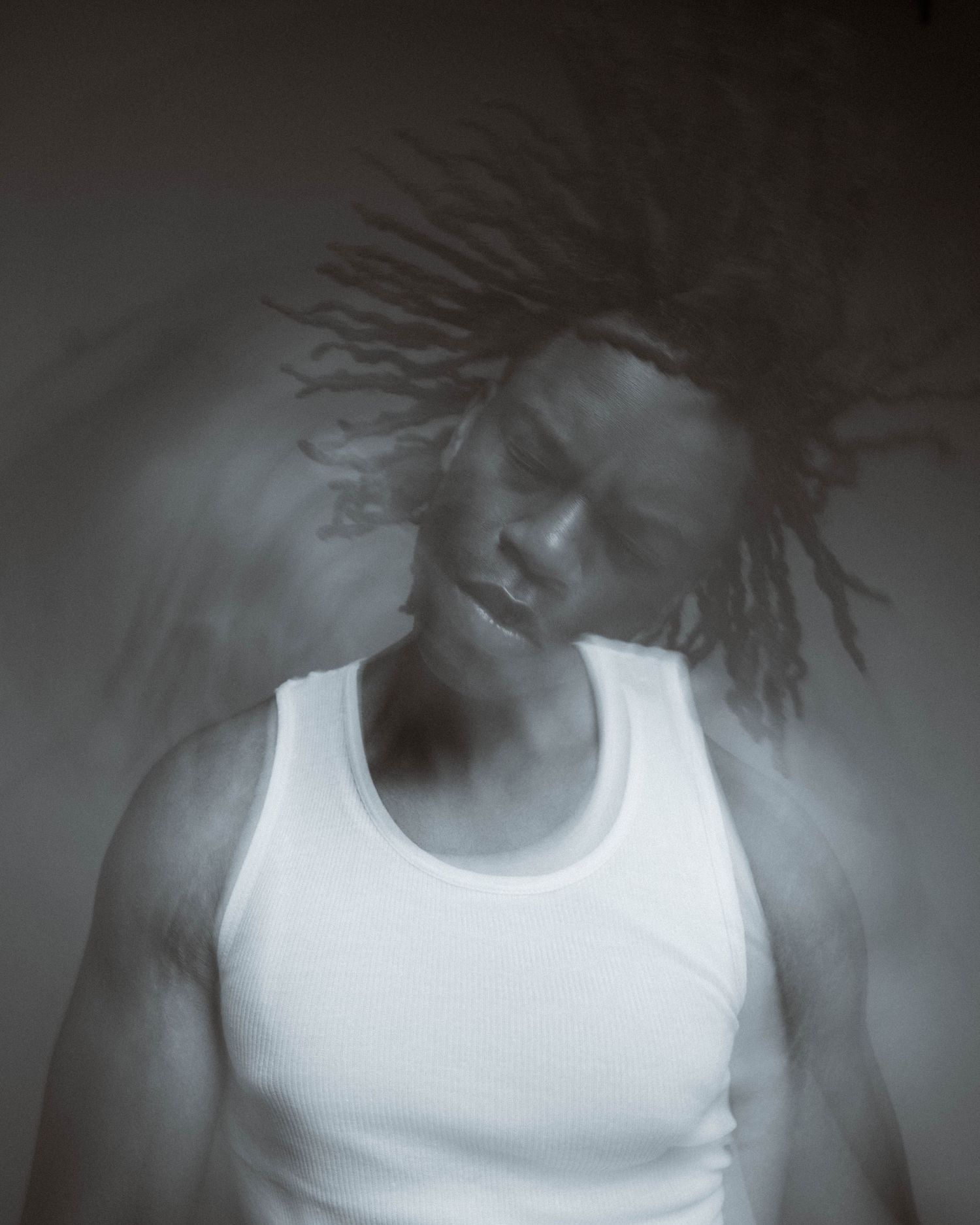 Artistic black and white portrait of a person with dreadlocks in a white tank top with eyes closed in contemplative pose.