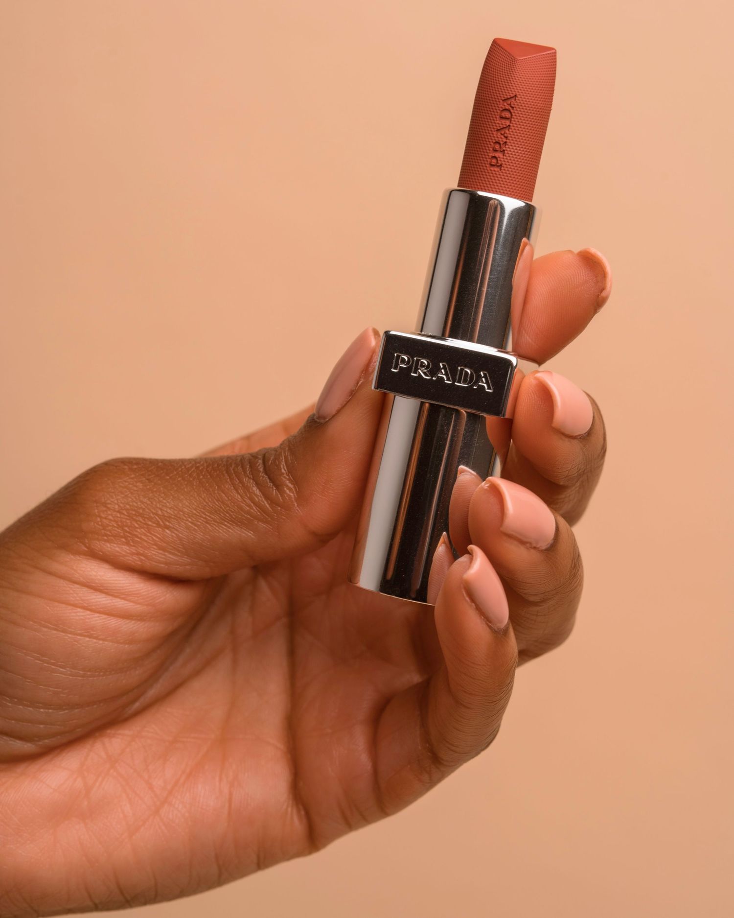 Hand holding metallic lipstick product against peach background.