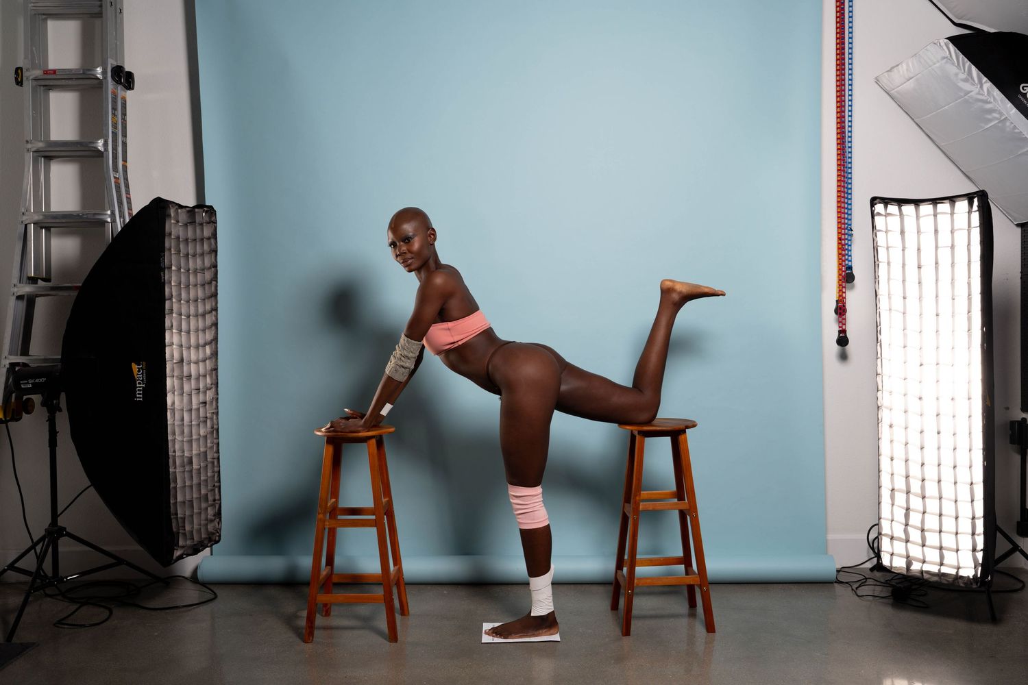 Modern dance poses utilizing wooden chair as prop against blue studio backdrop.