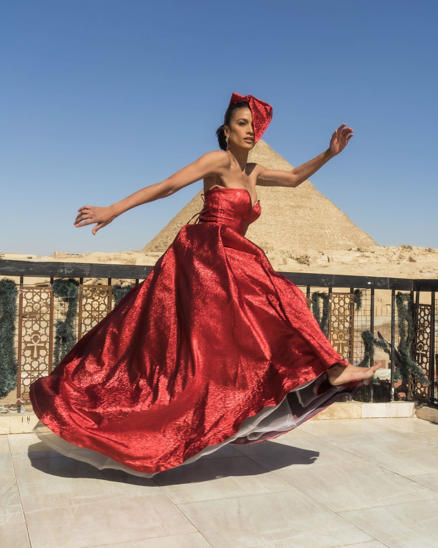 Dancer in red gown twirls gracefully with pyramid in background.
