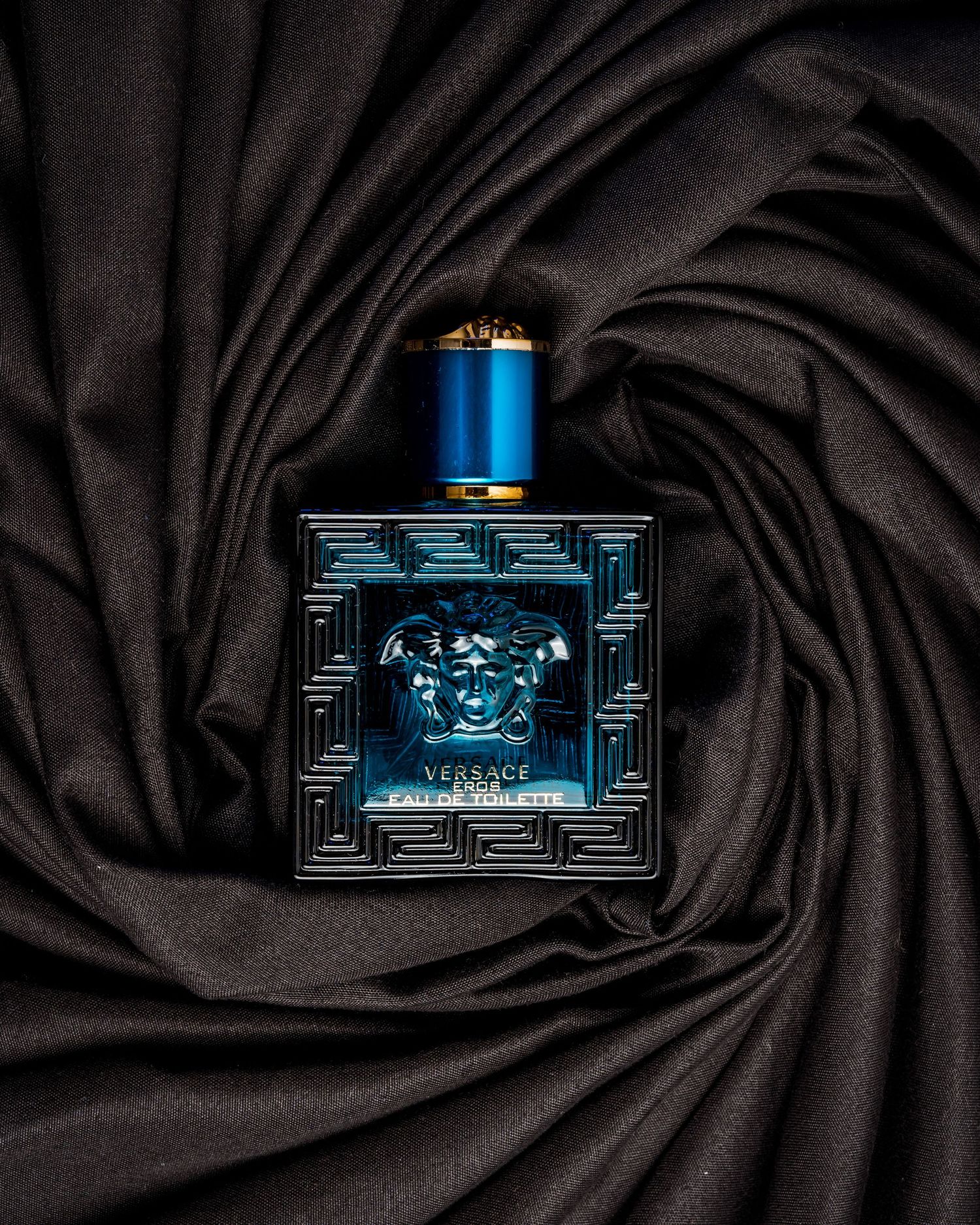 Designer fragrance bottle with metallic accents photographed on black fabric.