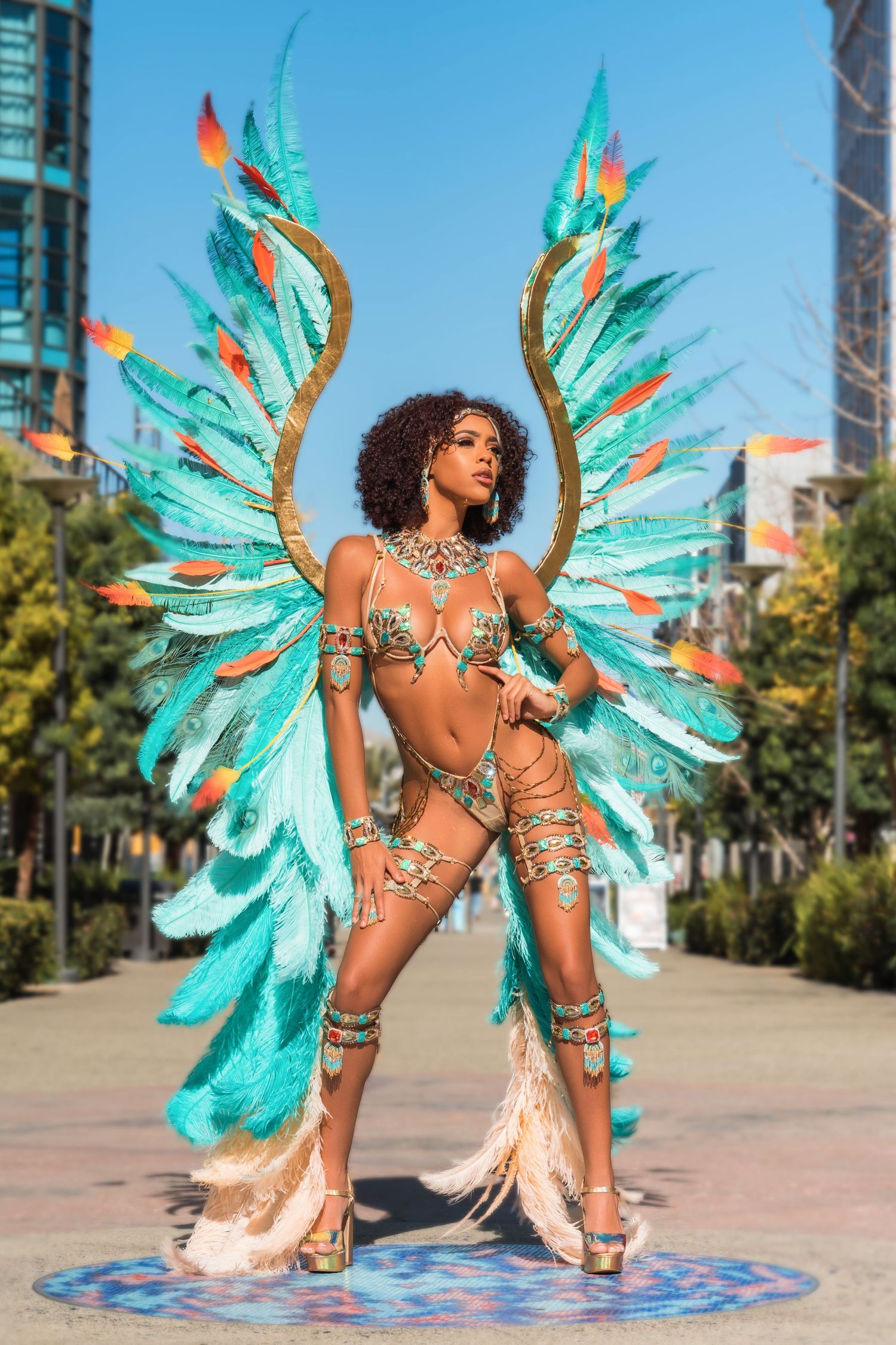 Dynamic carnival dance poses showcasing elaborate turquoise wing costume on decorative floor pattern.