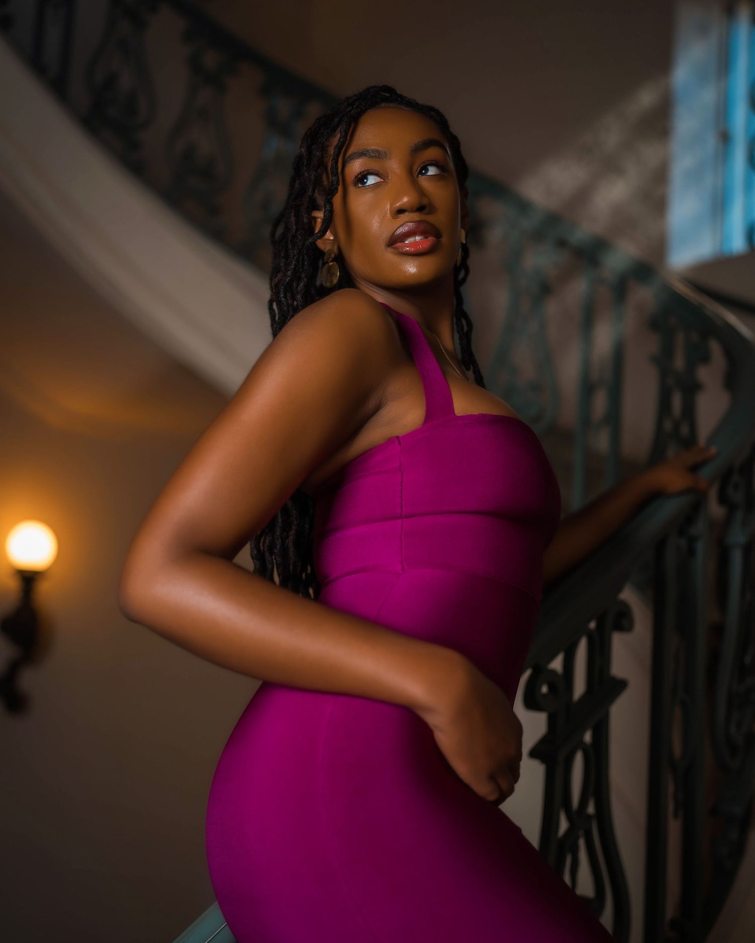 Woman in magenta dress poses gracefully in arched hallway.