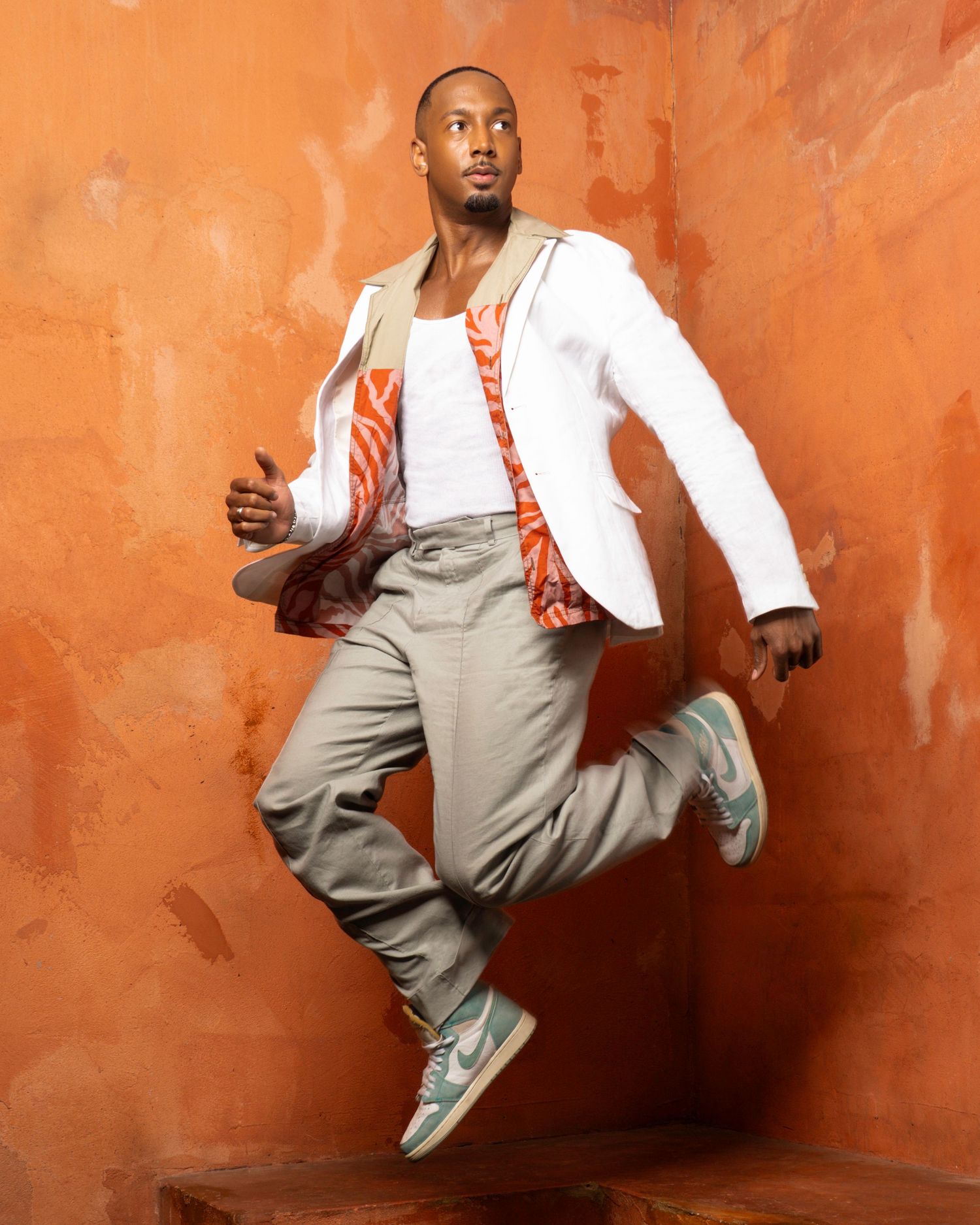Dynamic poses in white and beige outfit against textured orange wall.
