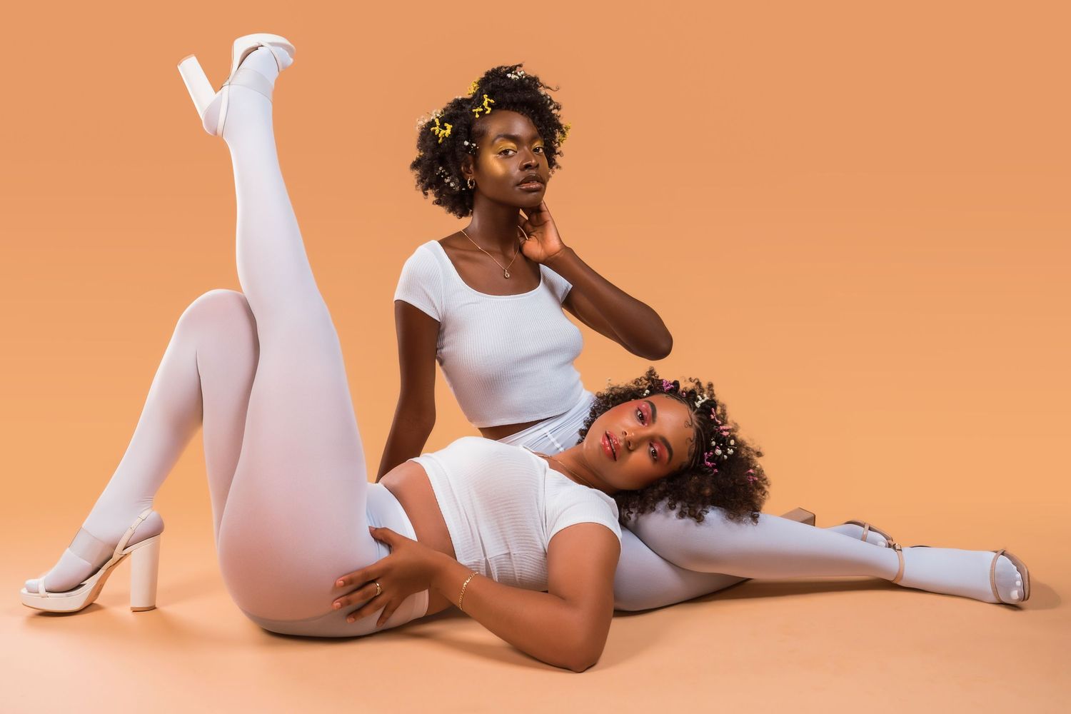 Models in white bodysuits create dynamic poses against peachy orange studio backdrop.
