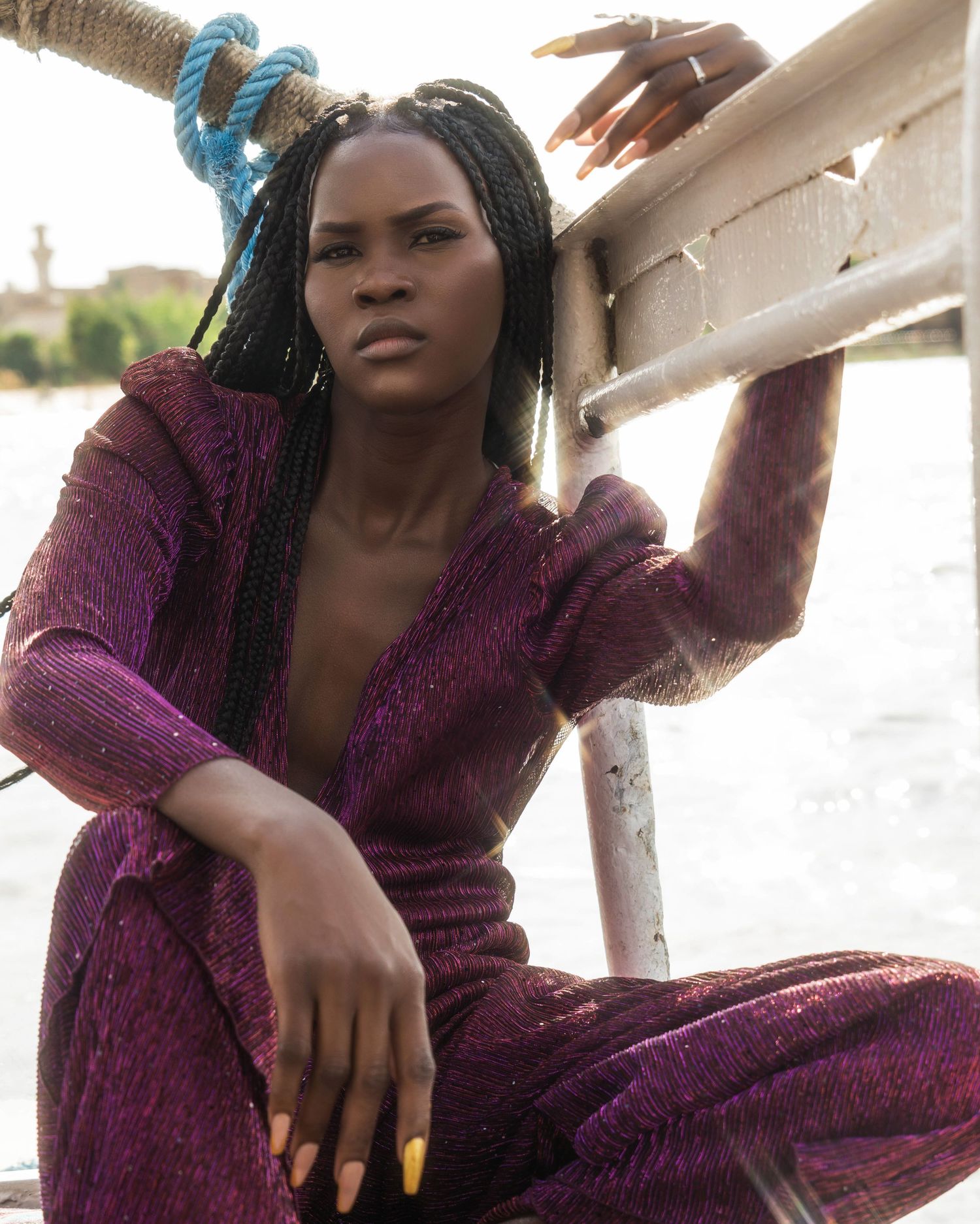 Model in plum sequined dress posing casually on boat railing.