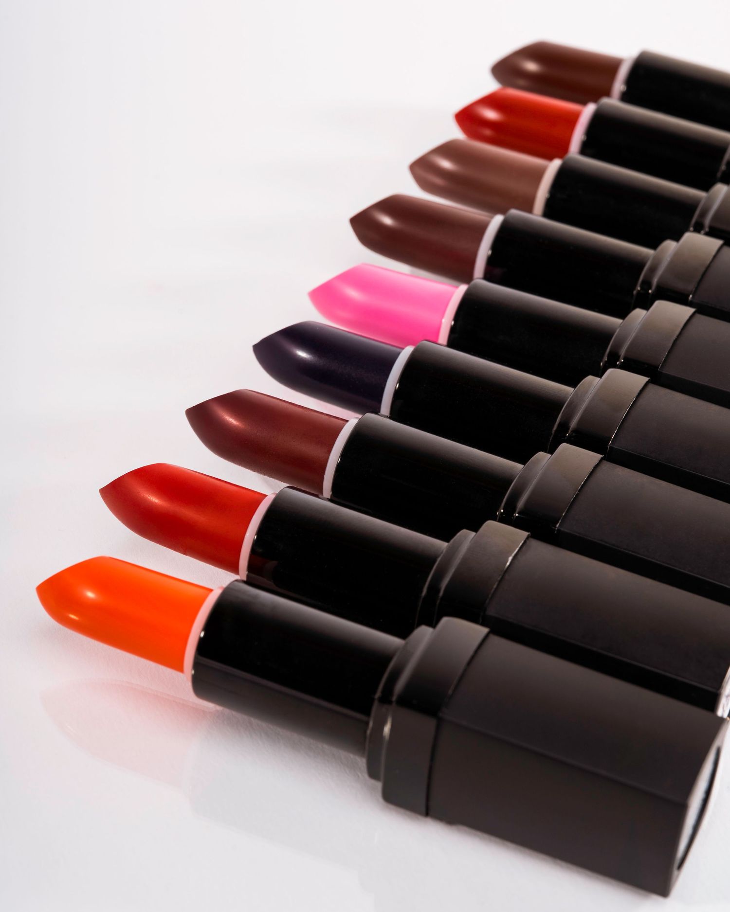 Row of lipsticks in various shades from red to pink arranged against white background.