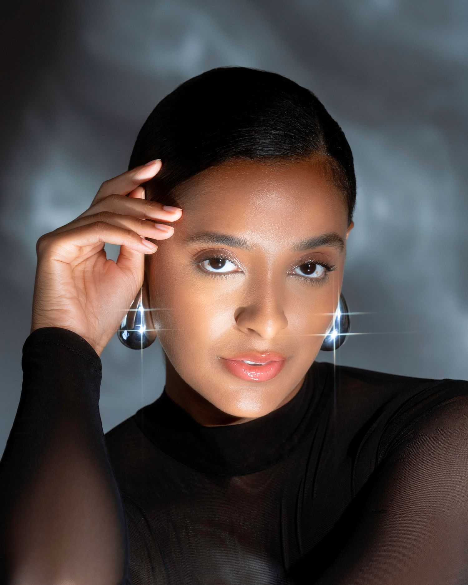 Glamour beauty portrait with sparkling earrings and sleek hair against moody backdrop.