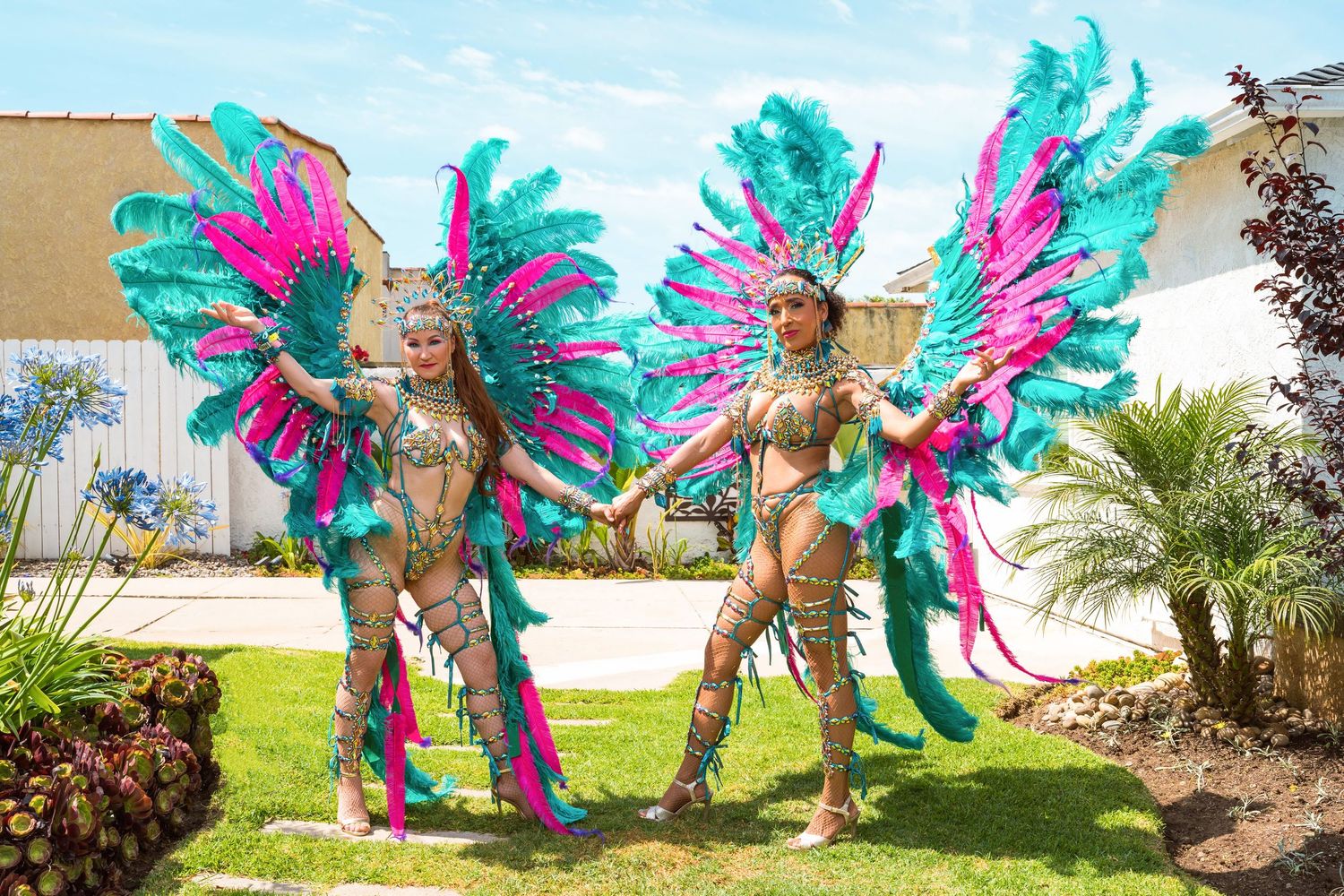 Dancers in colorful carnival costumes with feathered wings perform in a garden setting.