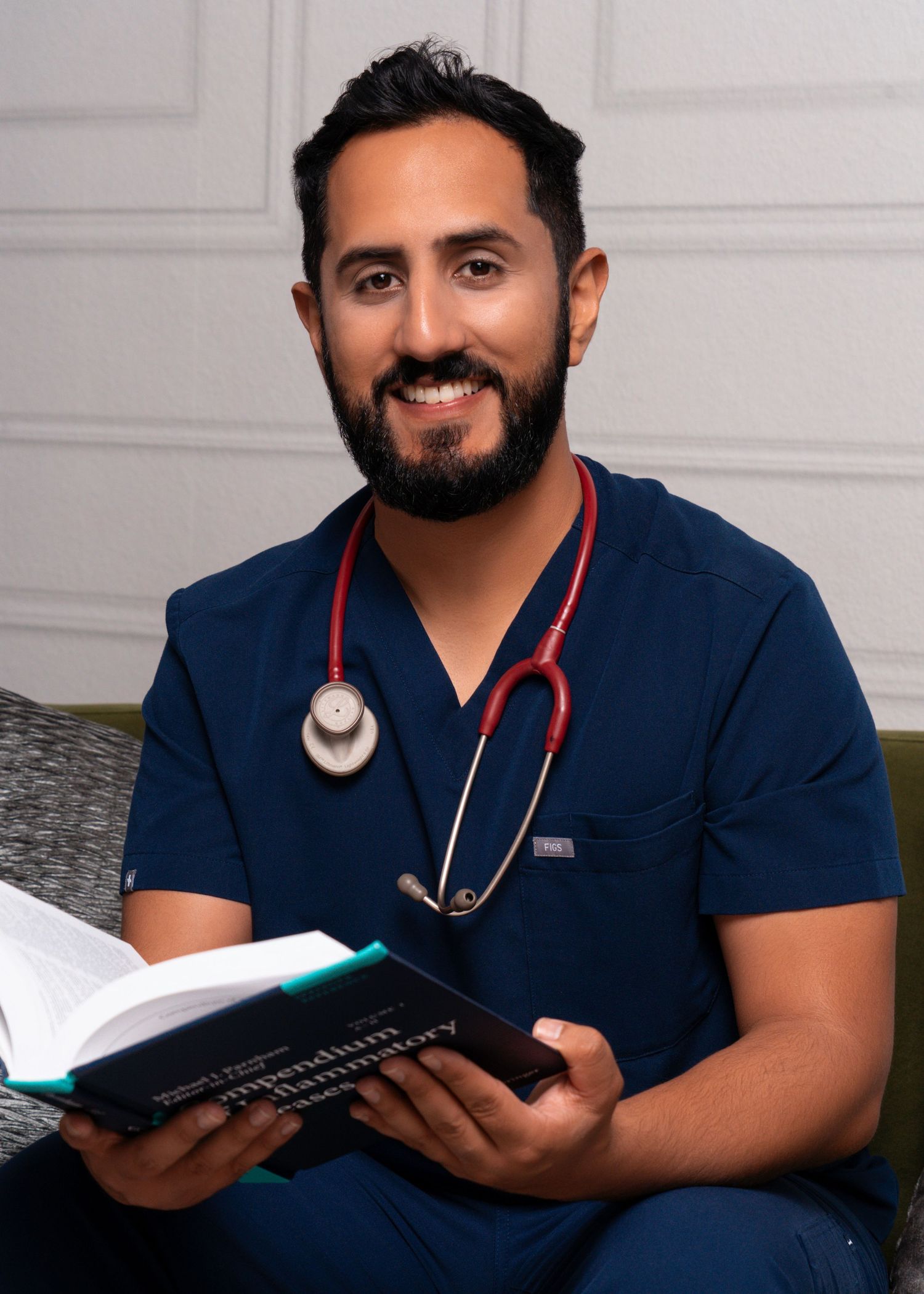 Healthcare provider in navy scrubs with stethoscope reading medical textbook.