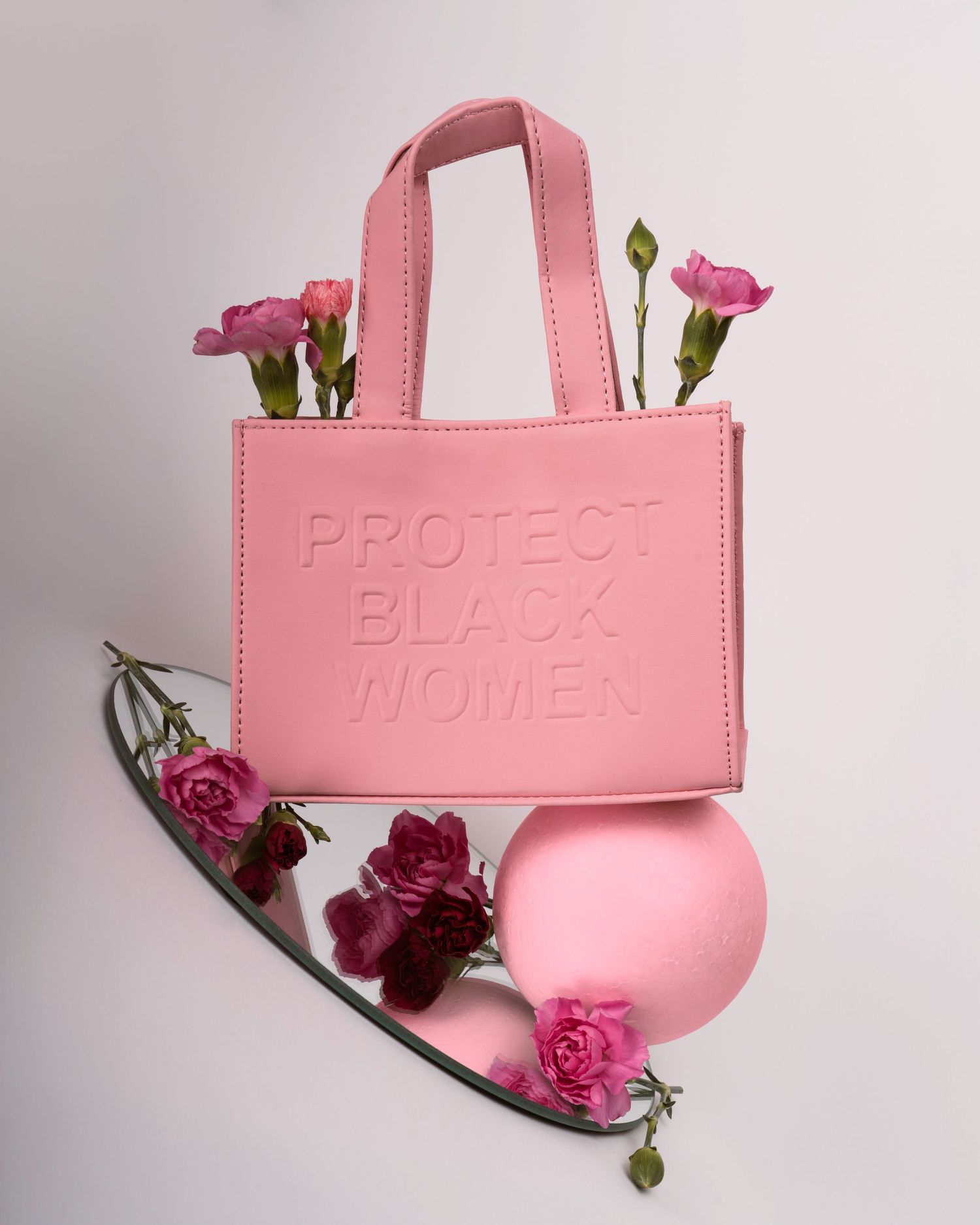 Pink leather tote bag with embossed text styled with roses on mirrored surface.