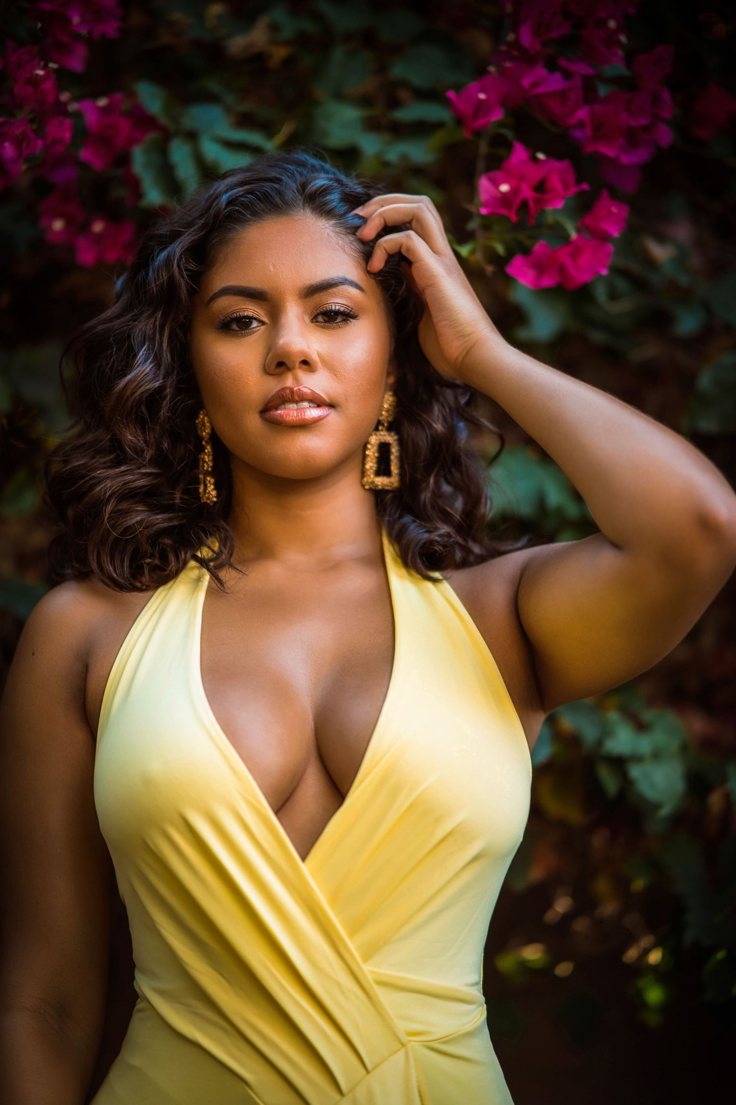 Woman in yellow halter dress with gold earrings posing before vibrant pink bougainvillea flowers.